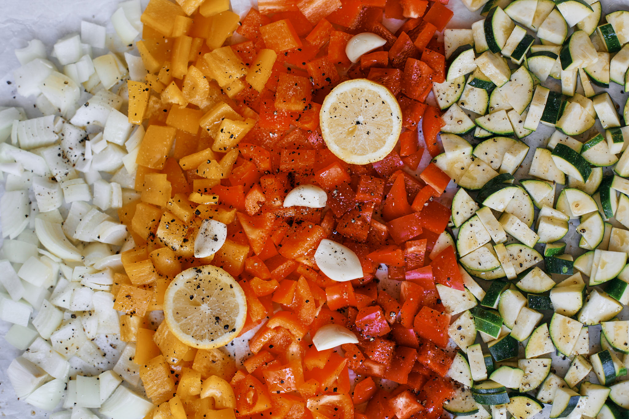 chopped zucchini, bell peppers and onion on a baking tray with parchment - covered with olive oil and salt and pepper