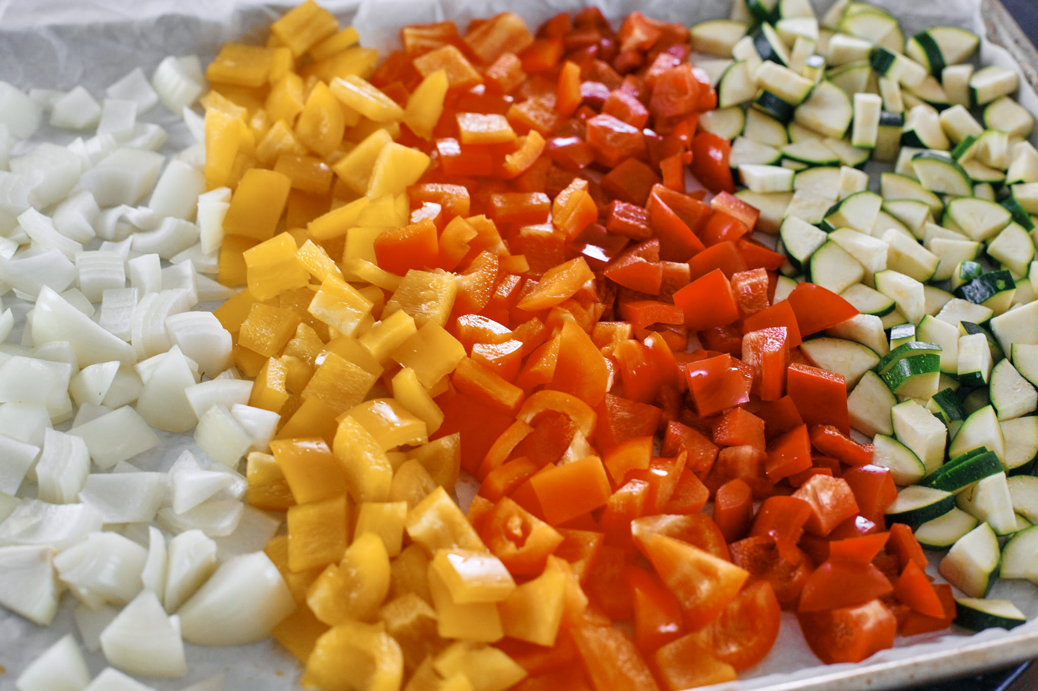 chopped zucchini, bell peppers and onion on a baking tray with parchment