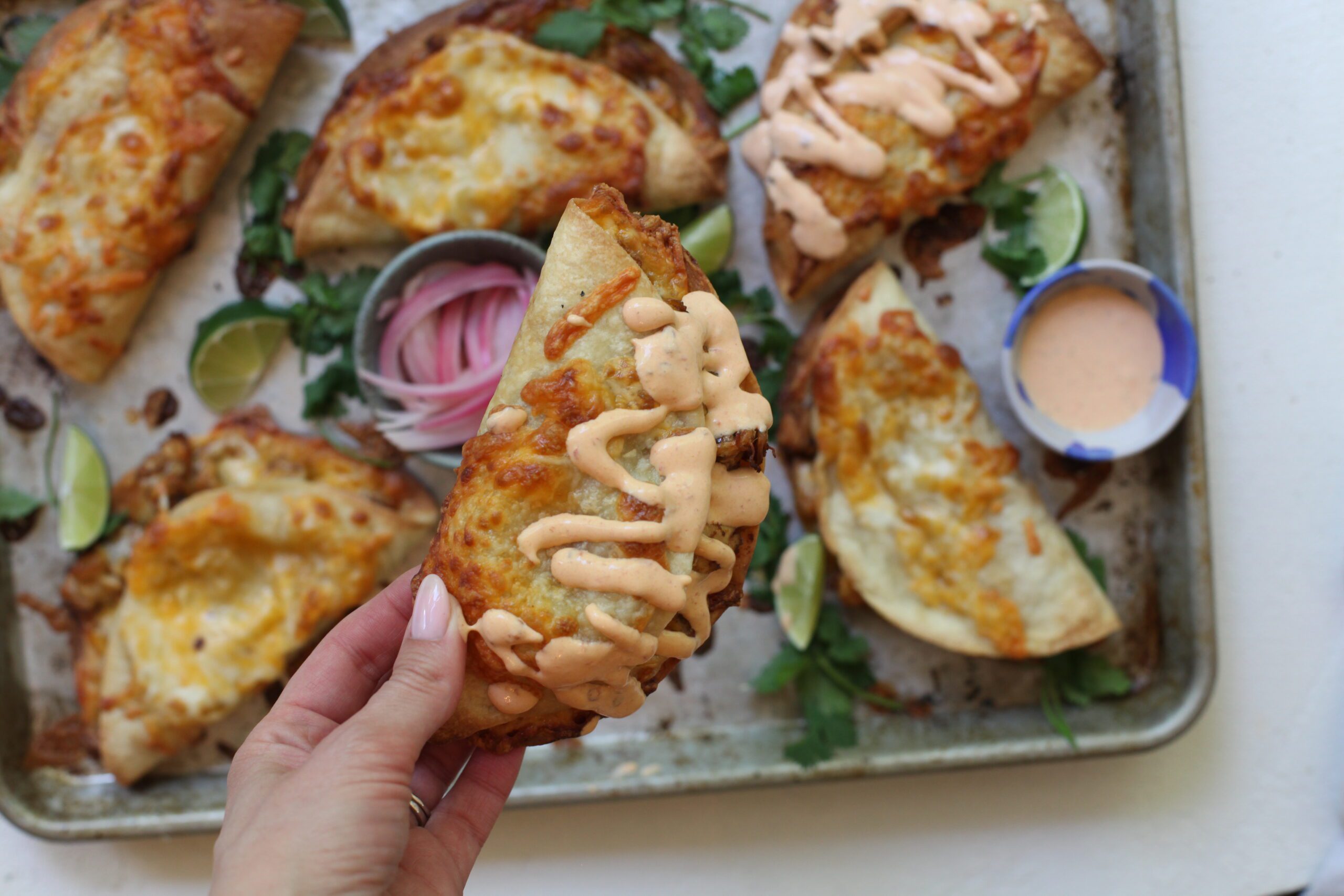 a hand holding a sheet pan chicken taco with chipotle crema