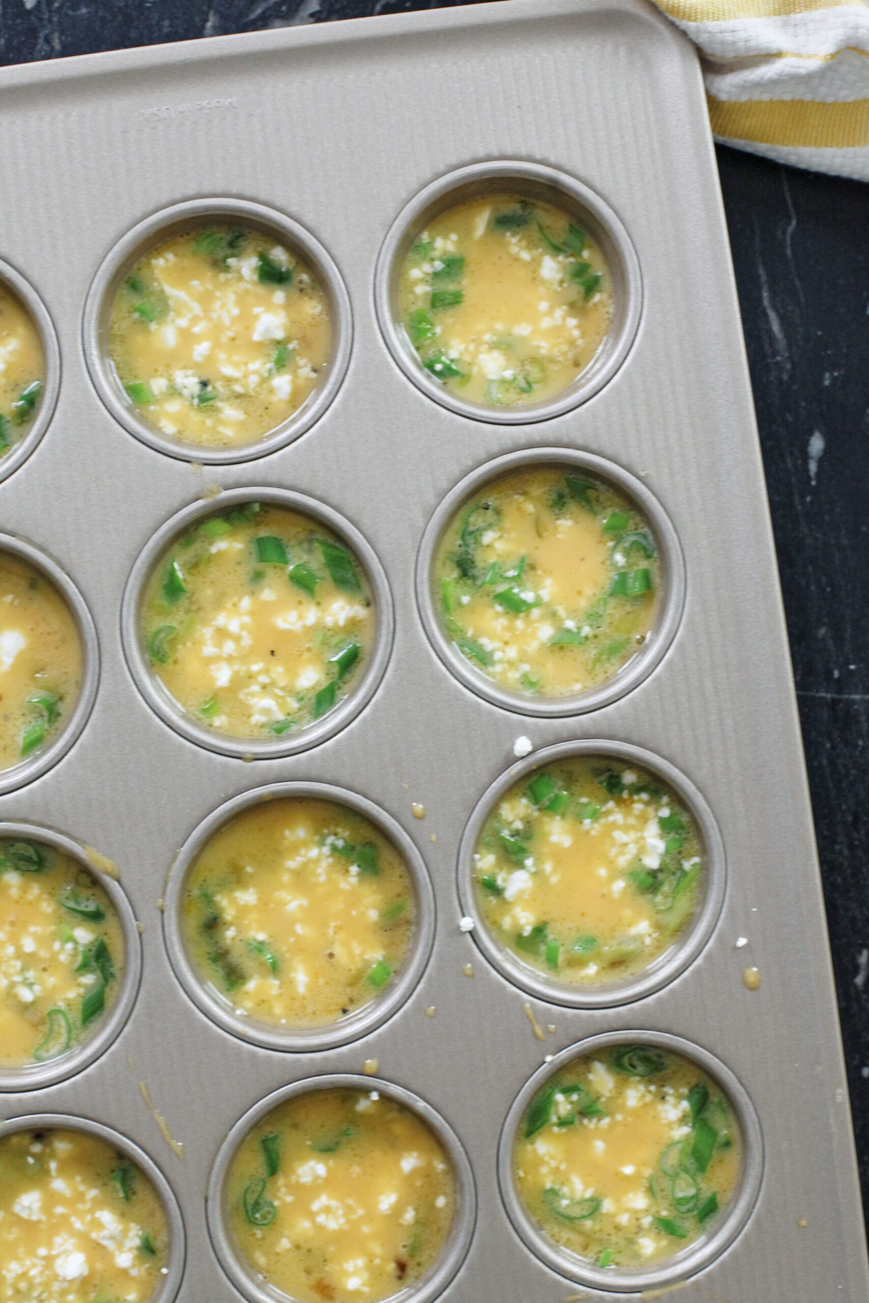 frittata mixture after being poured into a muffin tin and topped with feta cheese, before being baked