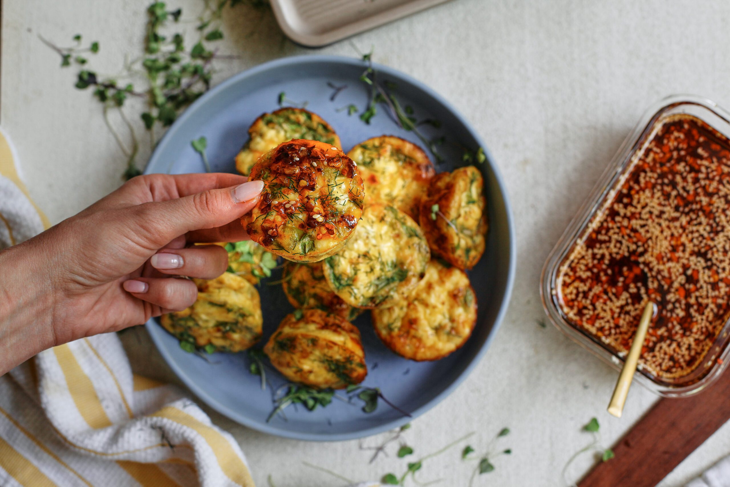a hand holding a mini spring frittata bite, topped with chili oil