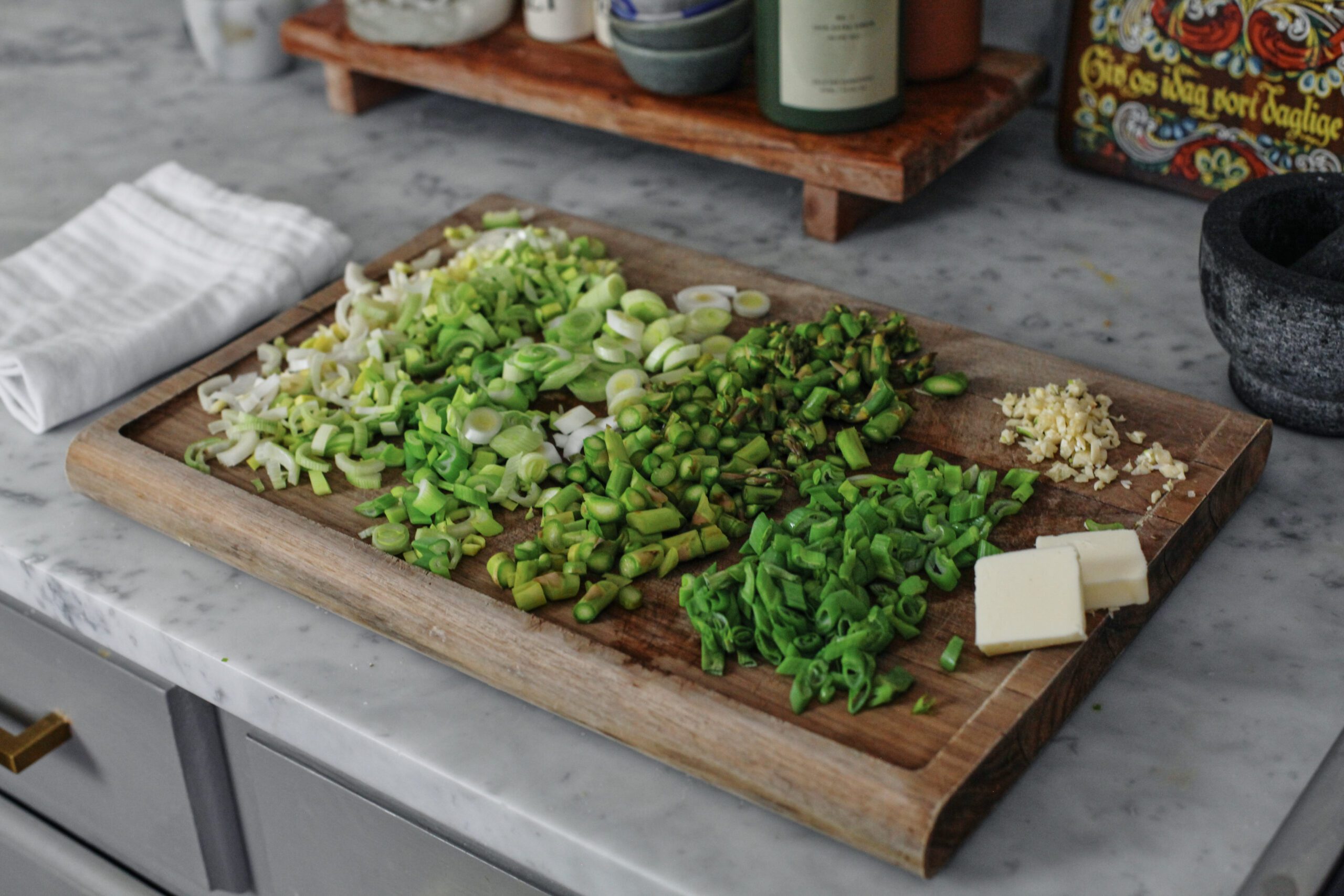 chopped leek, green onion, asparagus, and garlic on a cutting board wiht two knobs of butter