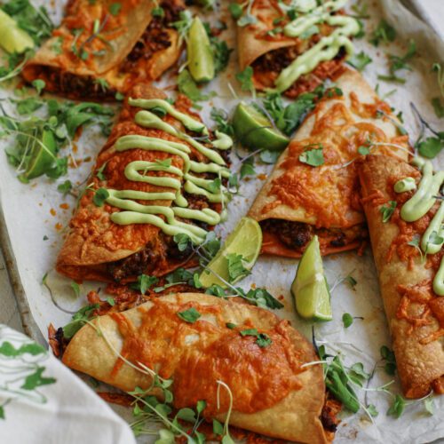 sheet pan beef tacos dressed with avocado lime crema, cilantro, and lime wedges