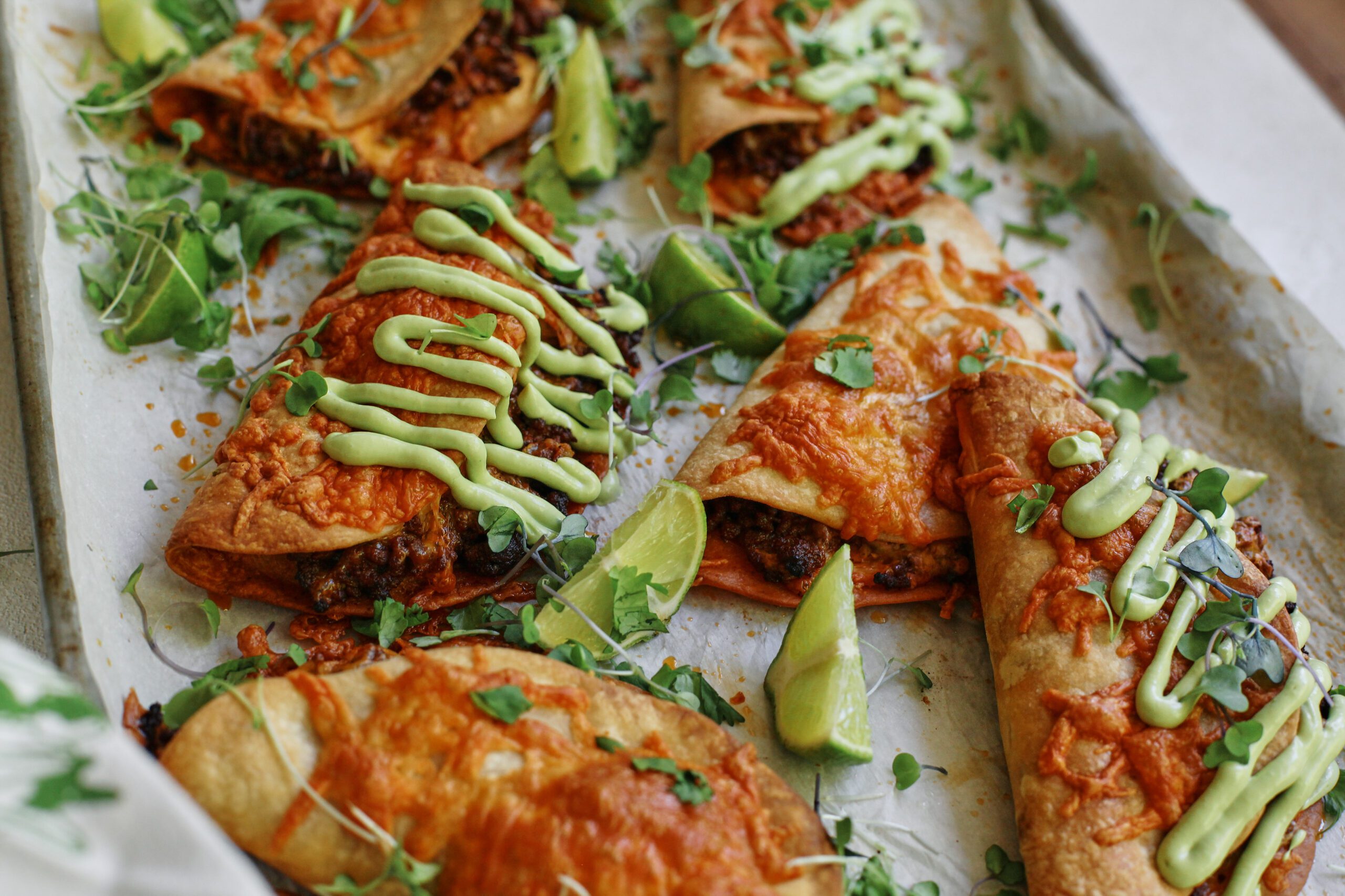 sheet pan beef tacos dressed with avocado lime crema, cilantro, and lime wedges