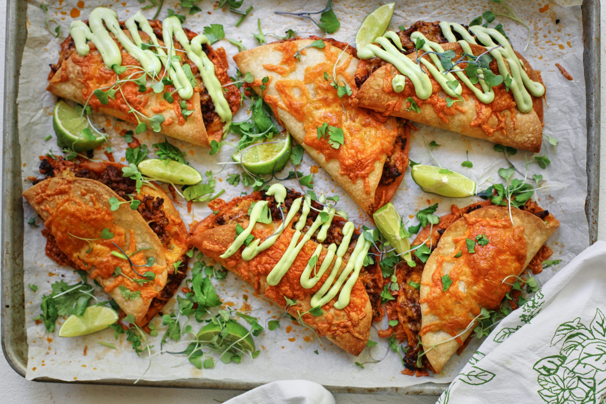 sheet pan beef tacos dressed with avocado lime crema, cilantro, and lime wedges