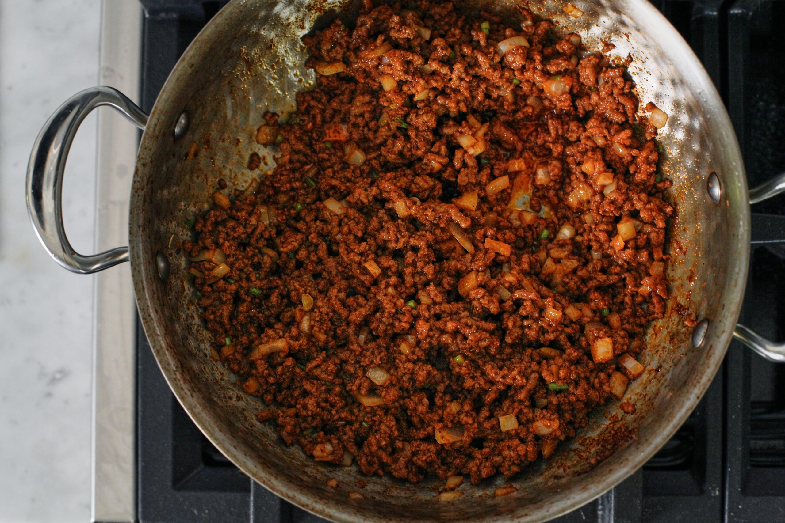 ground beef browned in a pan with spices, tomato paste, onion, and cilantro stems