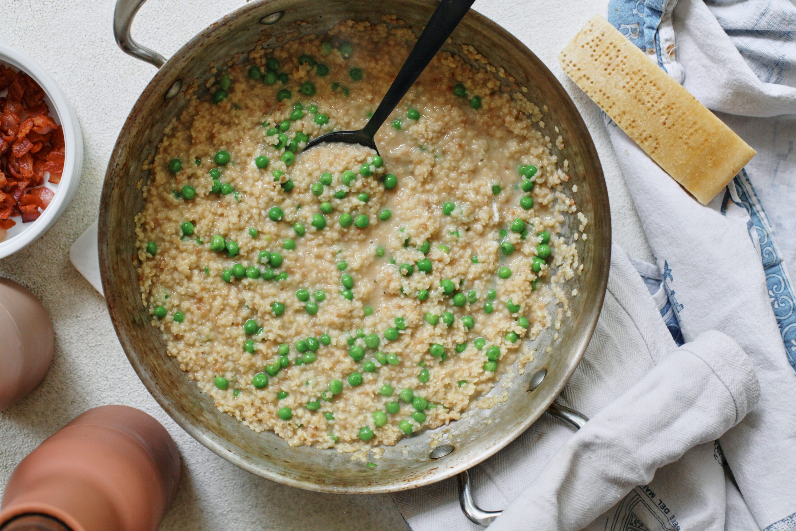 cooked cheesy pastina with peas in a pan with a serving spoon in the pan