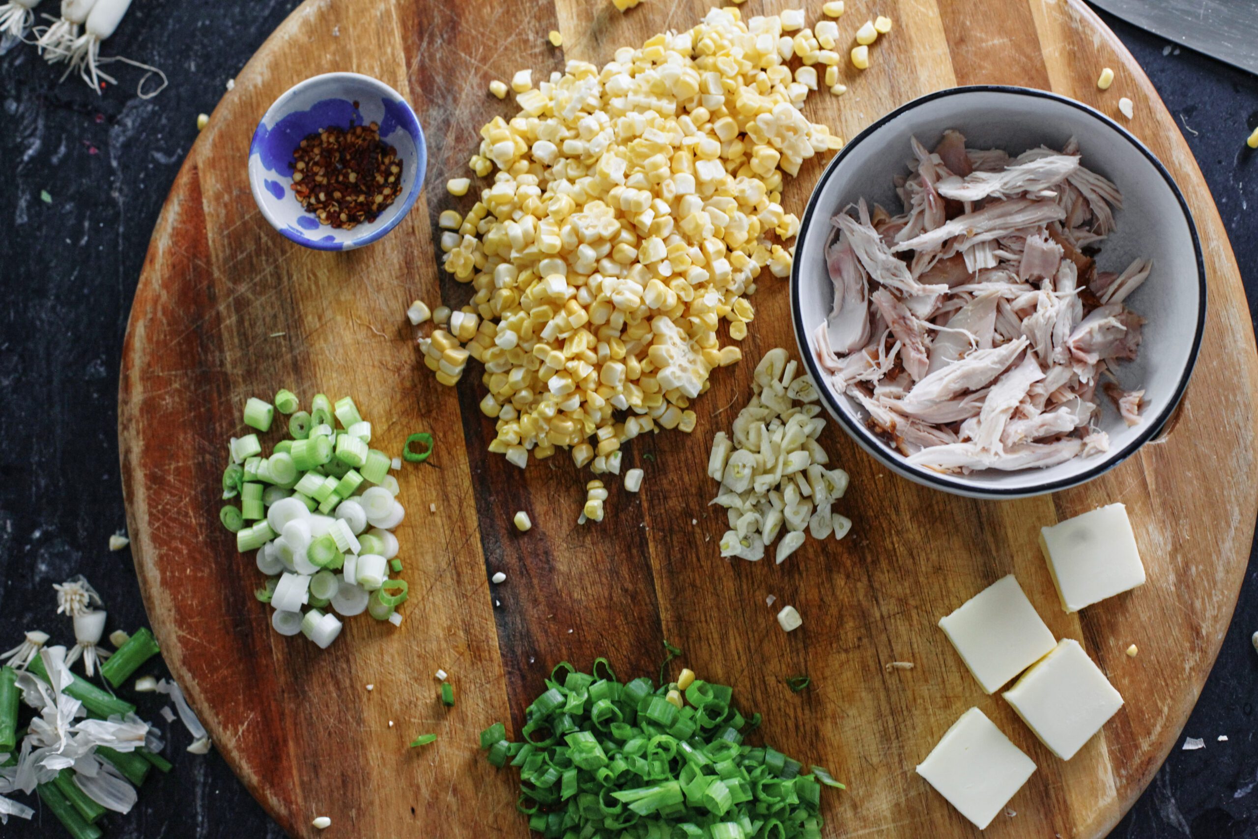 prepped ingredients for creamy corn and chicken pasta: red chili flakes, corn, rotisserie chicken, sliced garlic, butter, green onions