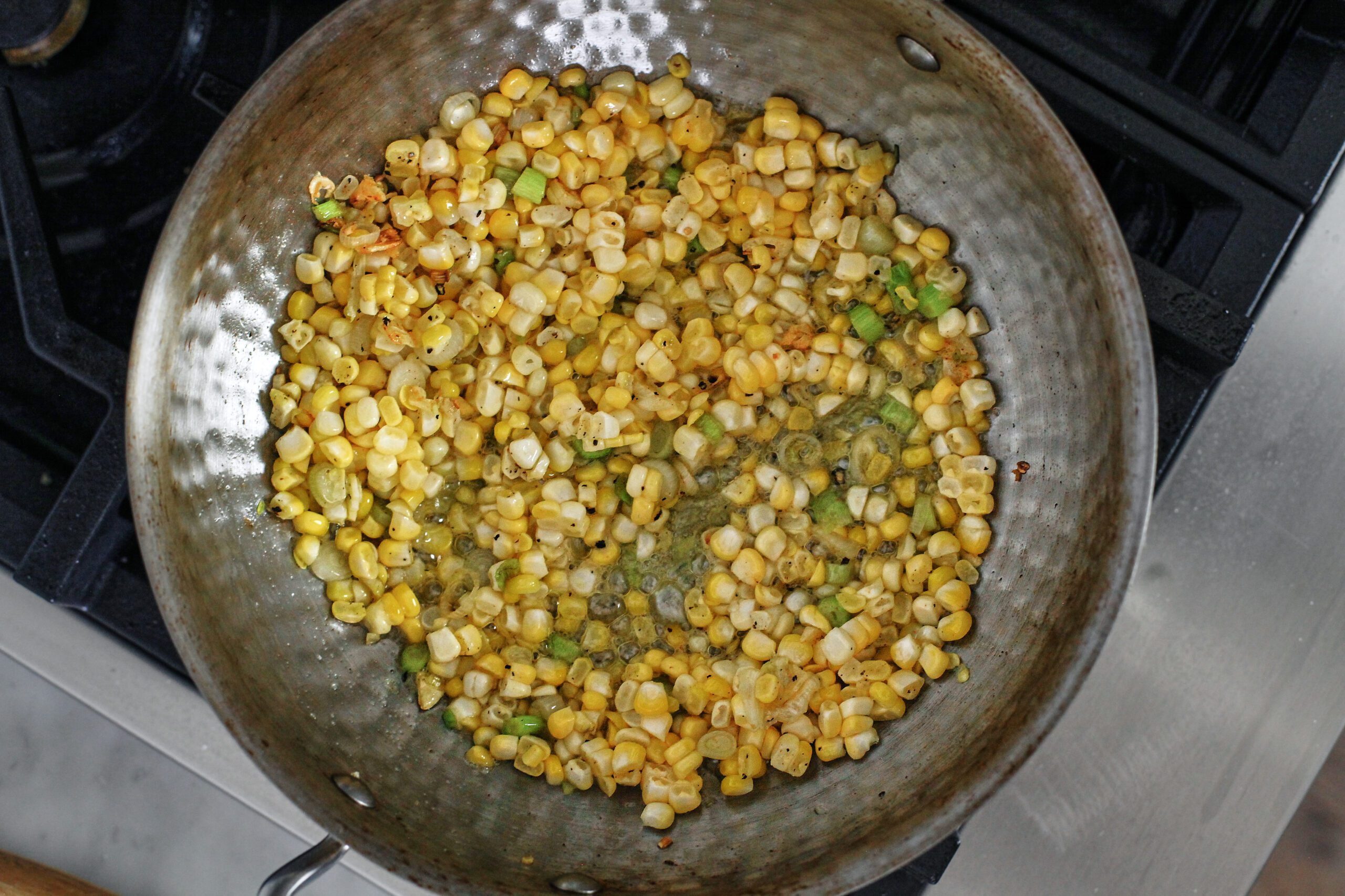 corn, green onions, and garlic sauteeing in a pan