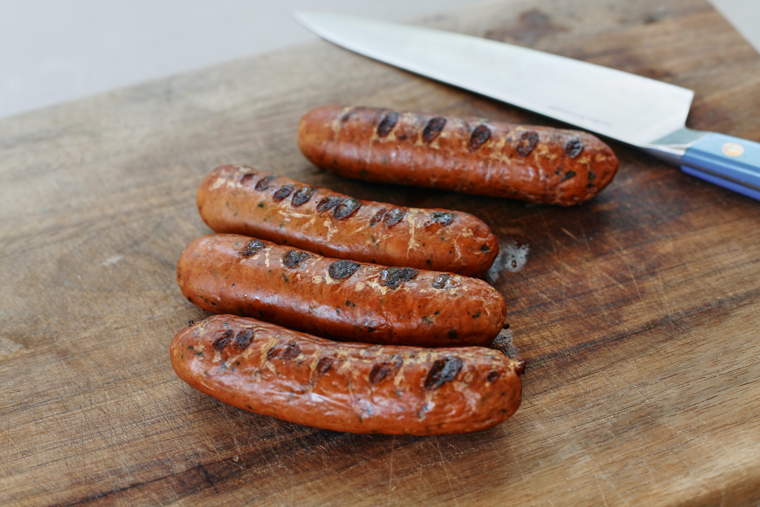 4 charred chicken sausages next to a knife on a cutting board