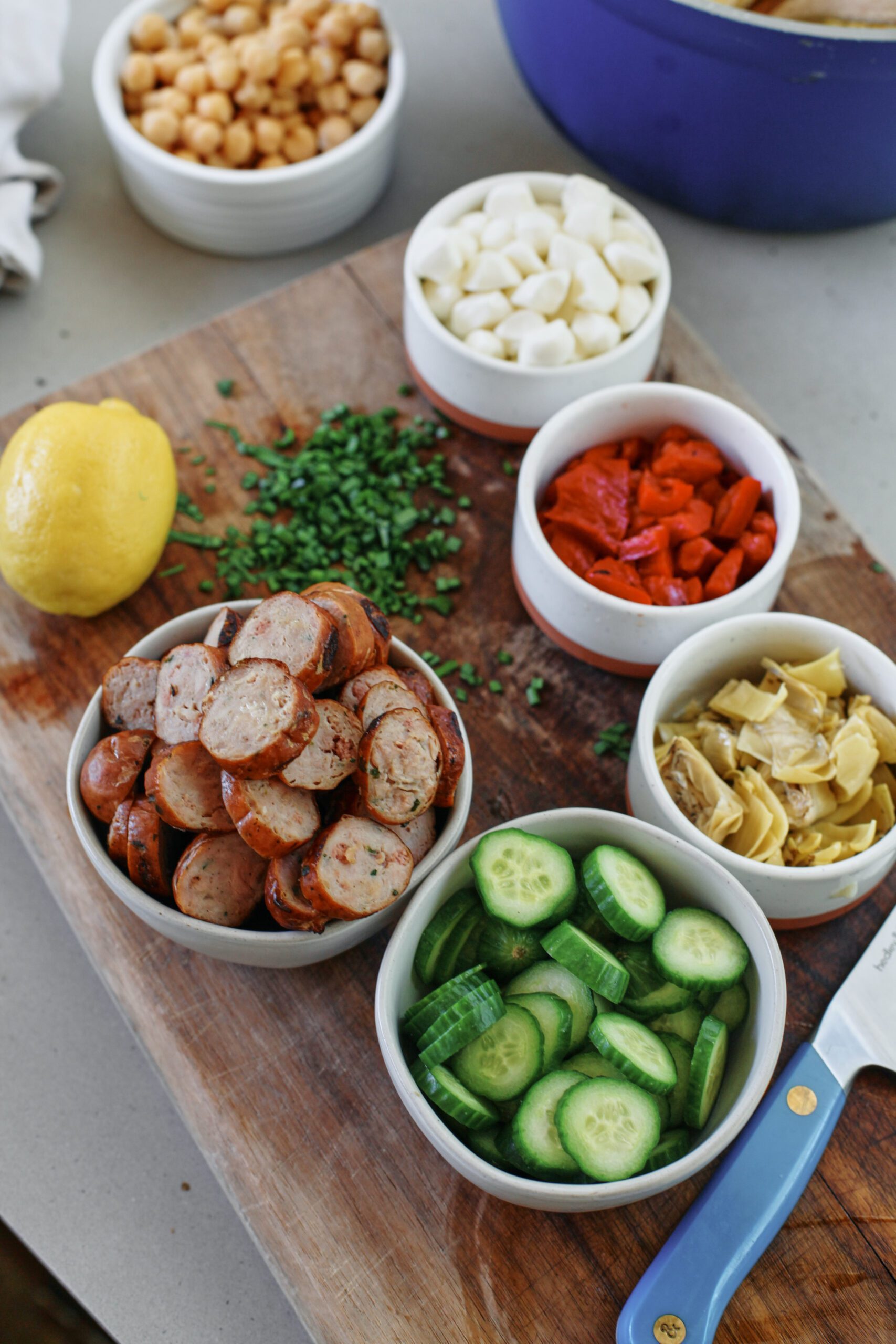 ingredients prepped and chopped for the salad: chickpeas, sausage, lemon, fresh herbs, mozzarella pearls, roasted red peppers, marinated artichoke hearts, cucumbers