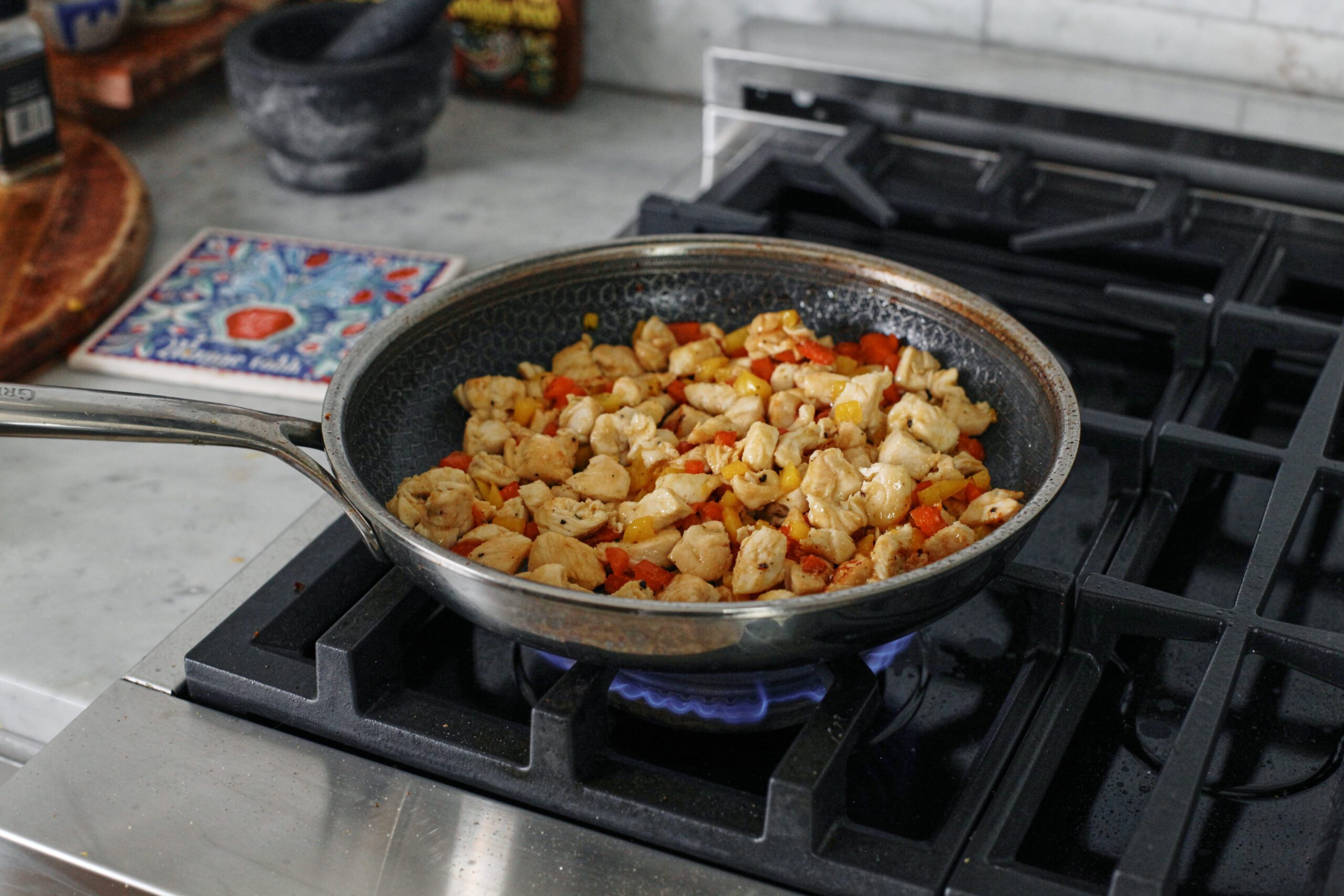 chopped chicken breat and chopped yellow and red bell peppers sauteeing in a pan on the stove