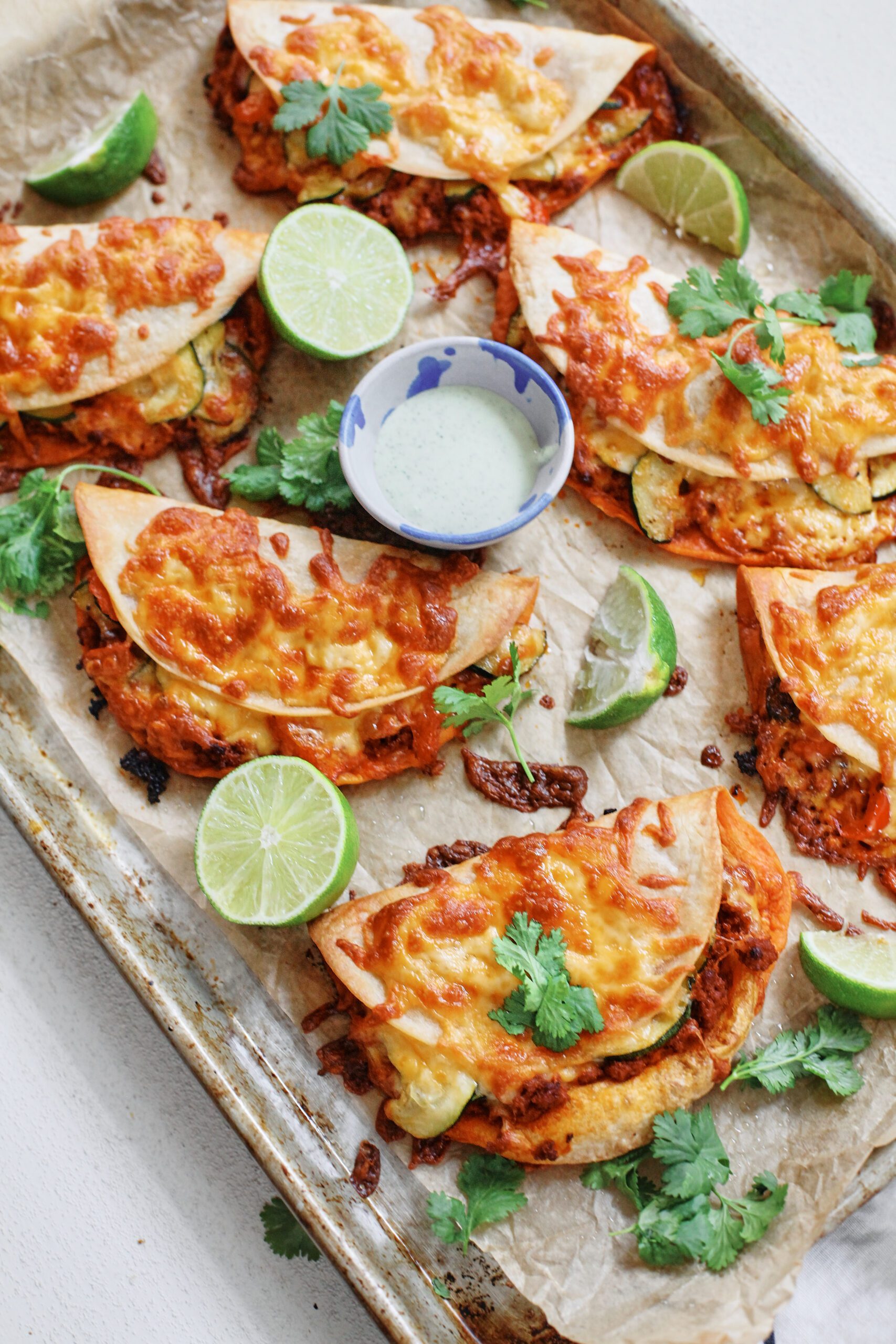baked chorizo sheet pan tacos served on a pan with limes, cilantro, and jalapeño garlic crema