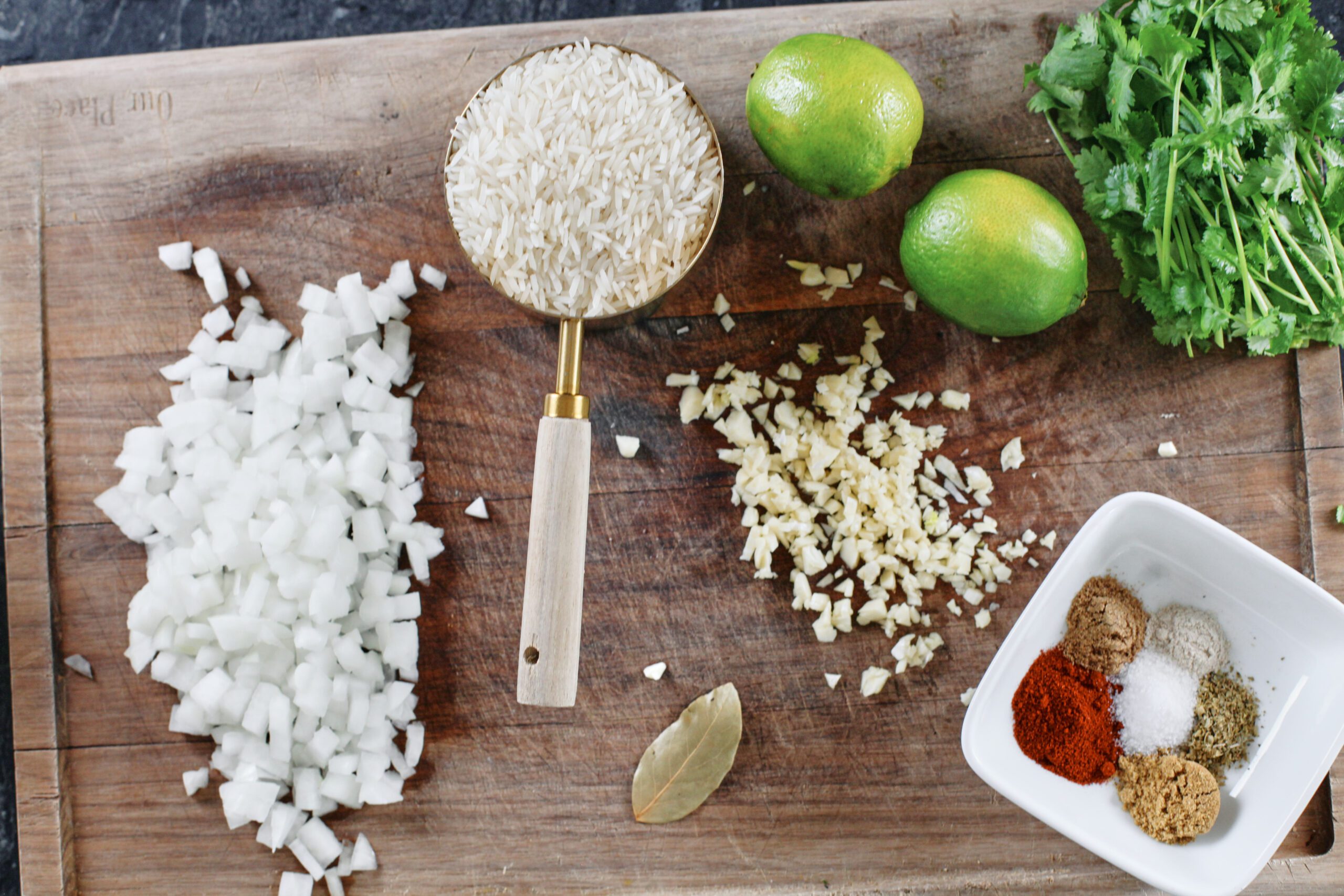ingredients prepped for soup: chopped onion, rice in a measuring cup, bay leaf, minced garlic, limes, cilantro, spice blend