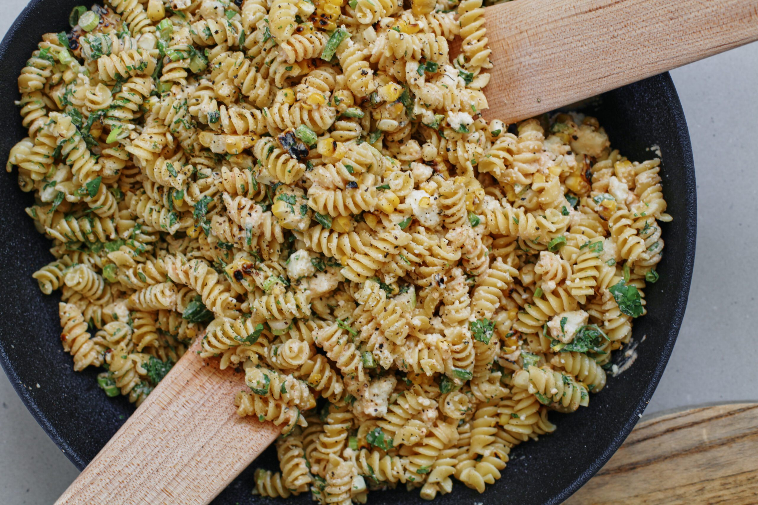 elote pasta salad after being mixed to combine in a large black bowl with wooden serving utensils