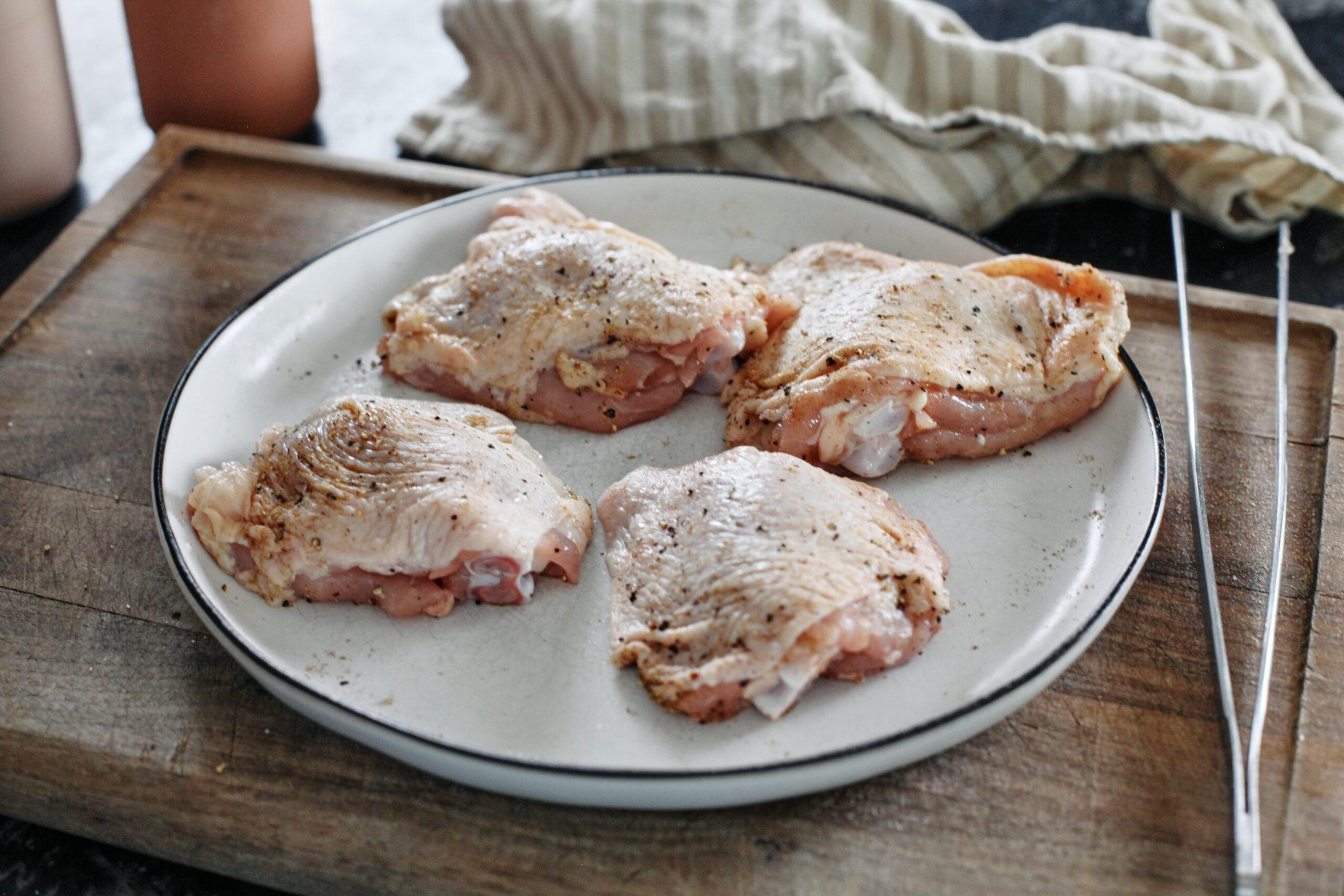 4 raw chicken thighs seasoned with salt and pepper on a white plate