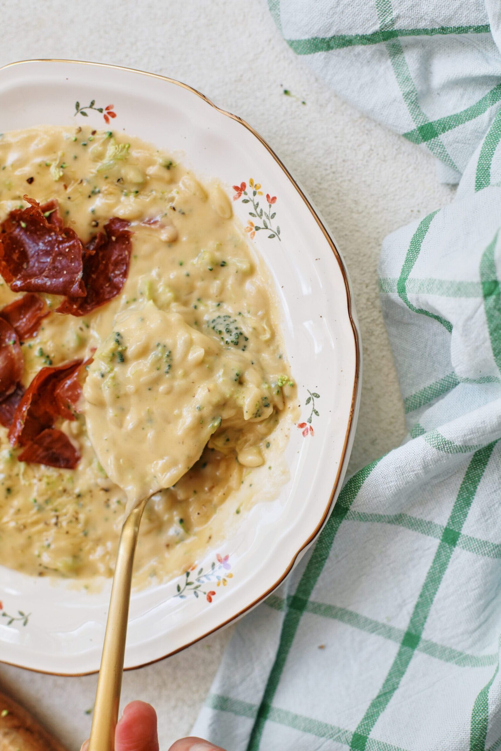 creamy broccoli cheddar orzo soup with crispy pancetta on top in a bowl