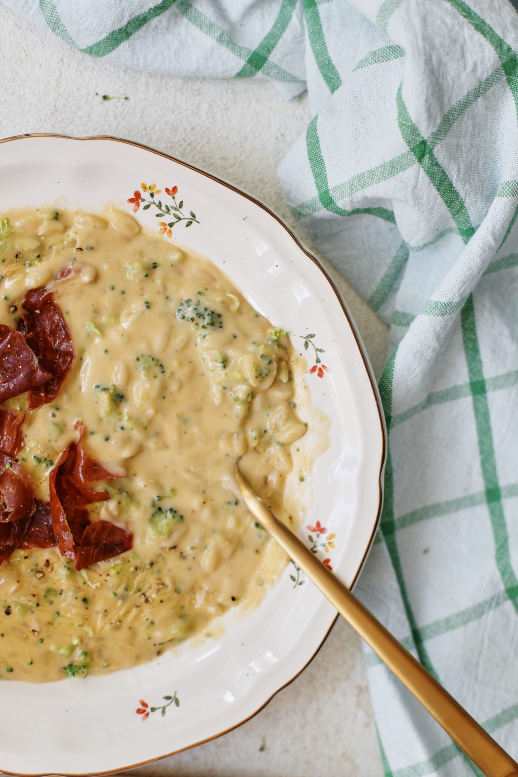 creamy broccoli cheddar orzo soup with crispy pancetta on top in a bowl