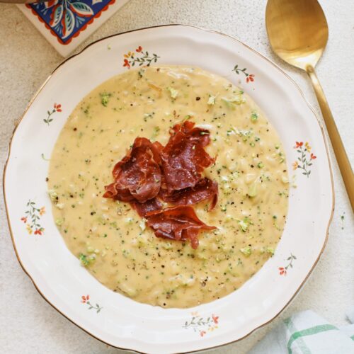 creamy broccoli cheddar orzo soup with crispy pancetta on top in a bowl
