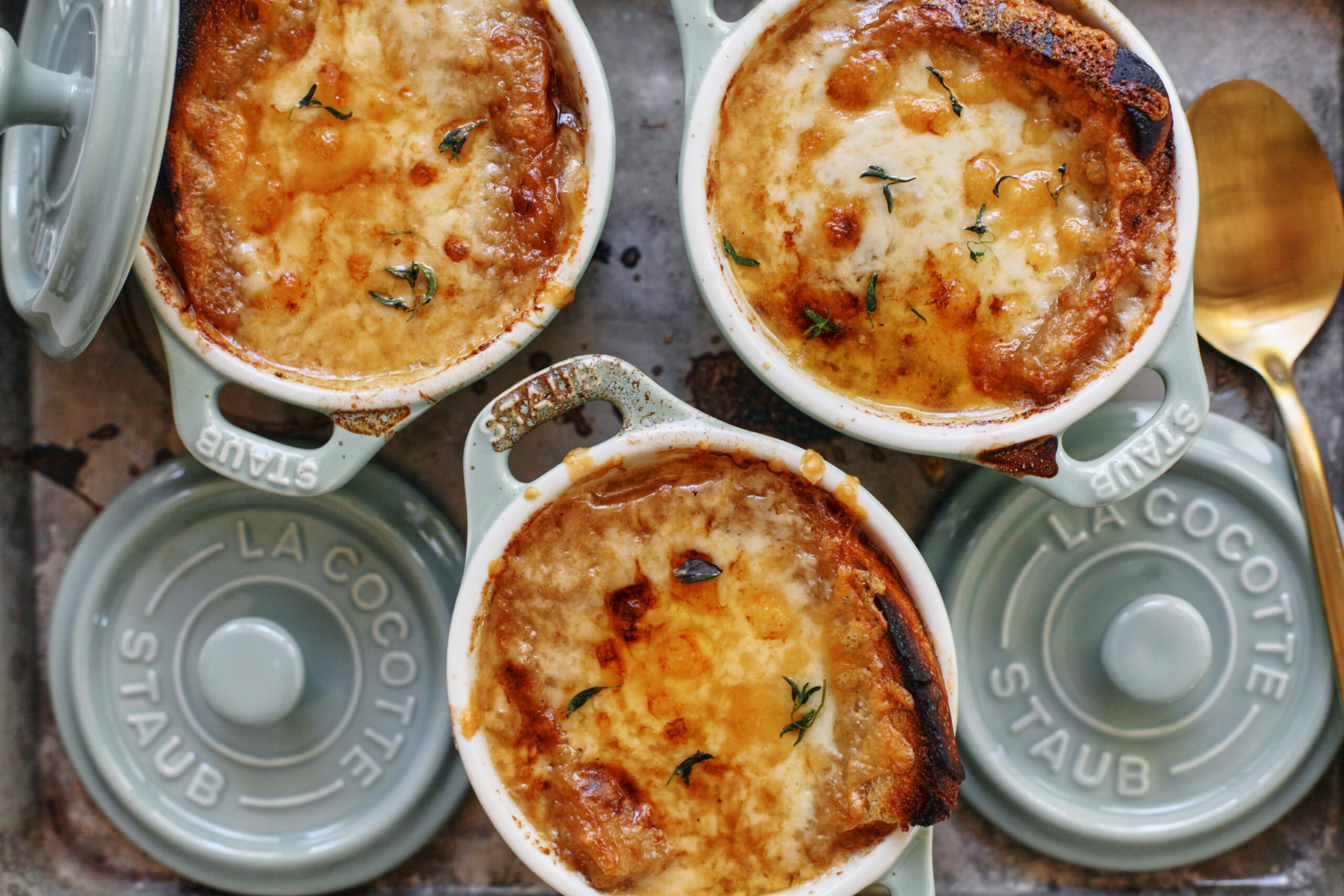 french onion soup in mini green dutch ovens that are arranged on a sheet pan, topped with golden, melted cheese