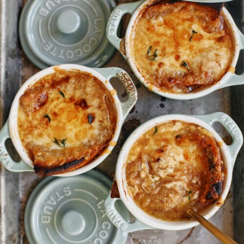 french onion soup in mini green dutch ovens that are arranged on a sheet pan, topped with golden, melted cheese