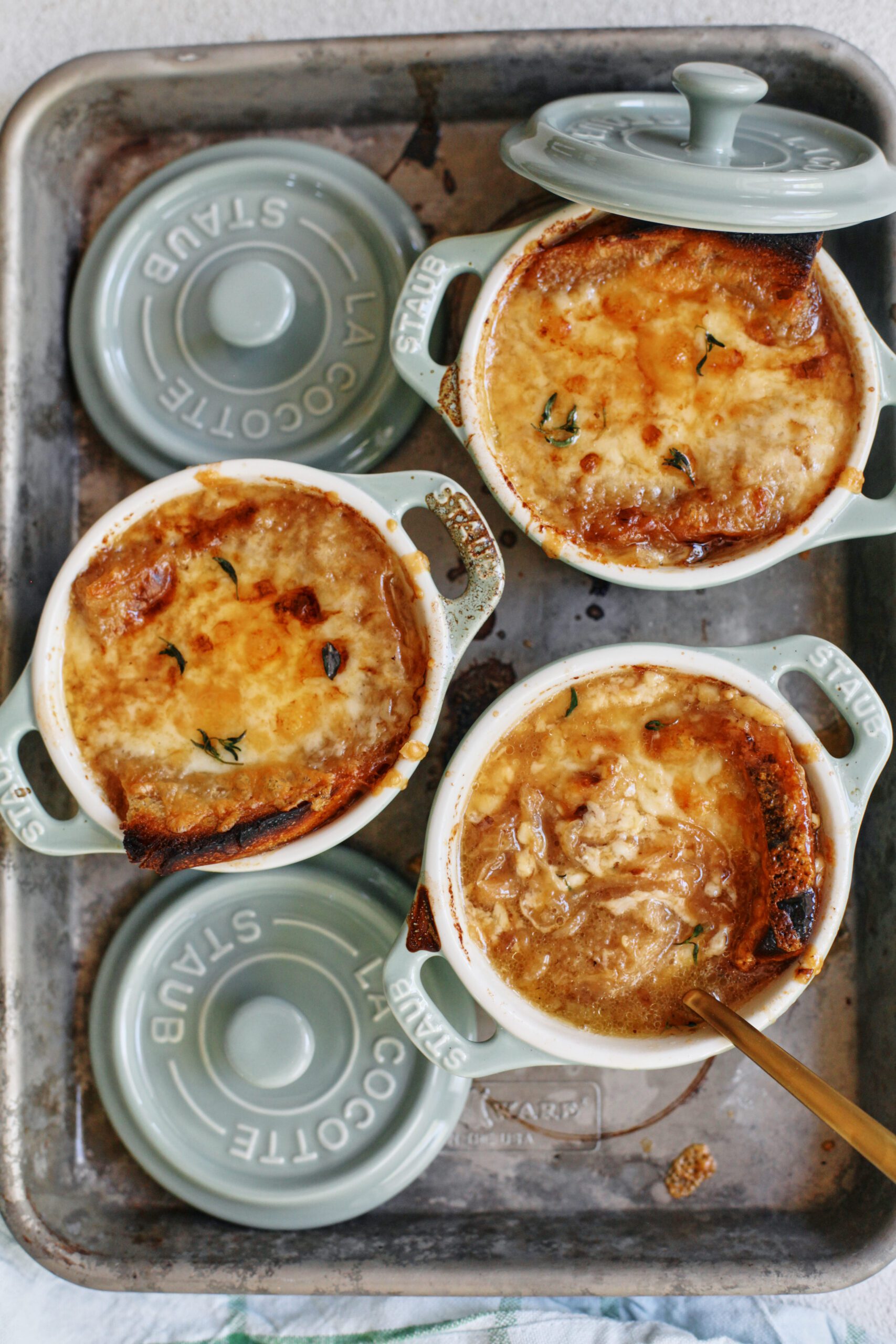 french onion soup in mini green dutch ovens that are arranged on a sheet pan, topped with golden, melted cheese