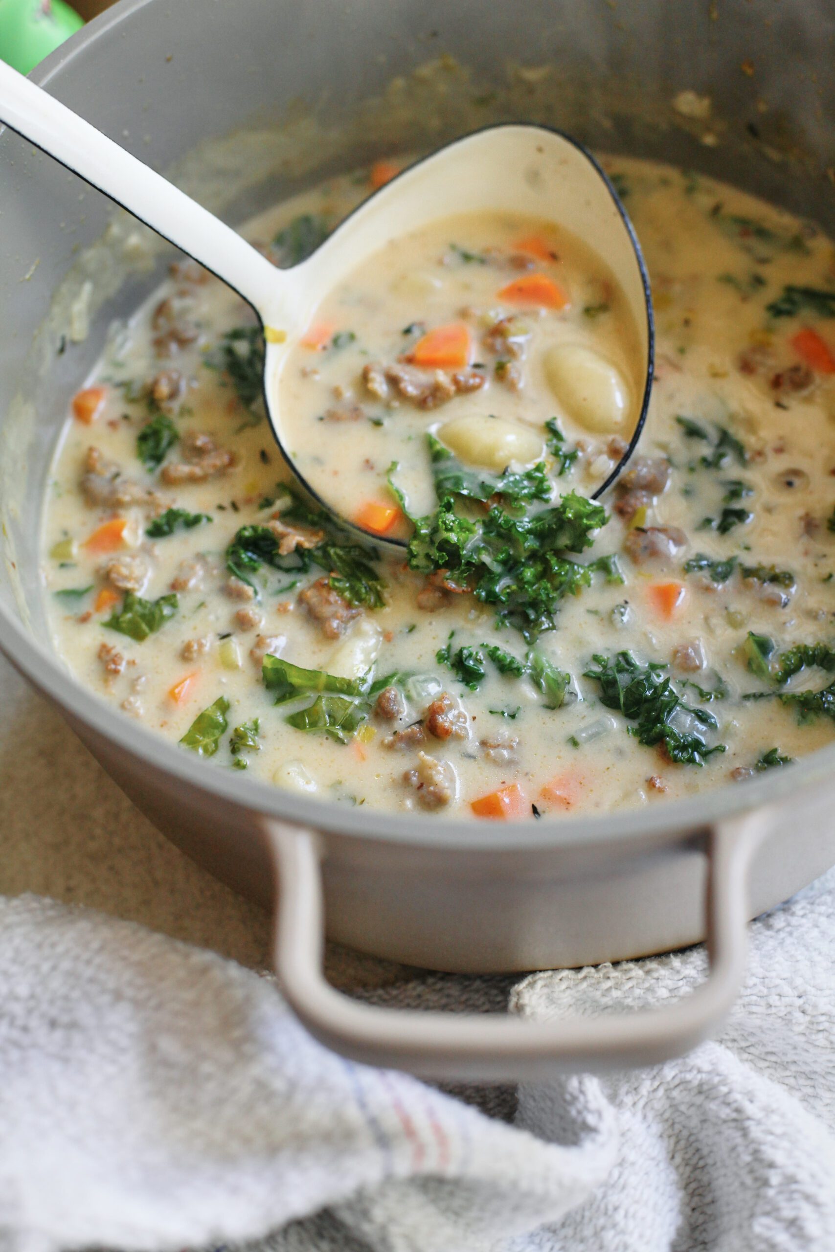 creamy gnocchi & sausage soup in a large pot with a white ladle
