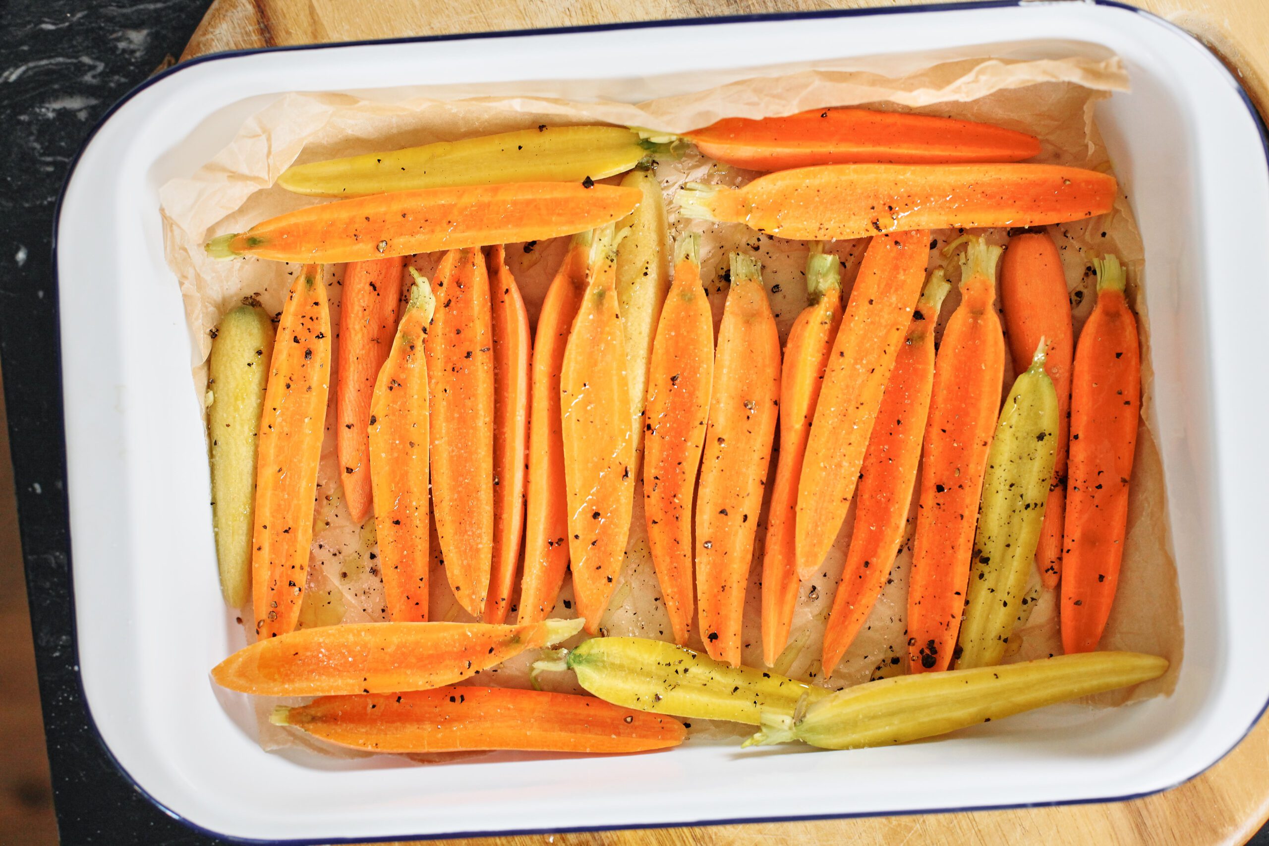 small orange and yellow carrots sliced down the middle, then arranged in a parchment-lined roasting pan