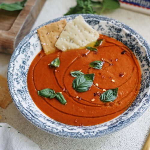 Roasted Red Pepper & White Bean Soup in a white bowl with a blue floral pattern, garnished with basil, olive oil, red pepper flakes, and Firehook Rosemary Sea Salt Crackers