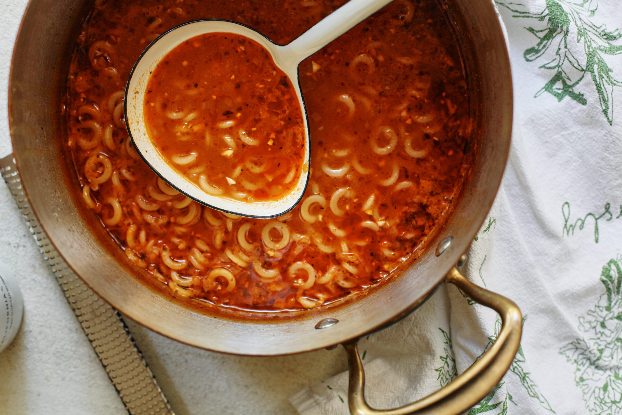 a large pot of brothy parmesan spaghetti soup with a white ladle