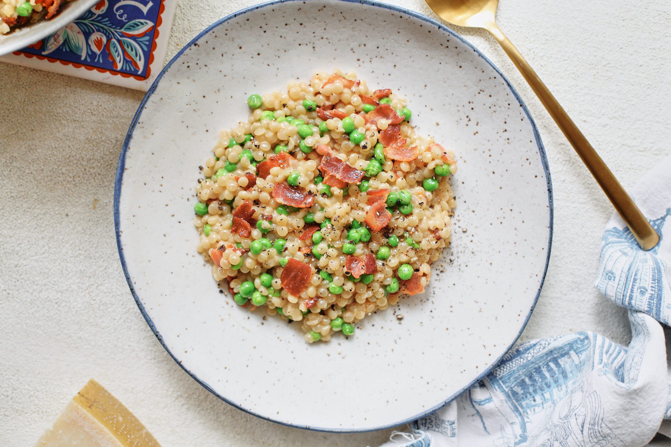 pearl couscous with bacon & peas served into a white bowl