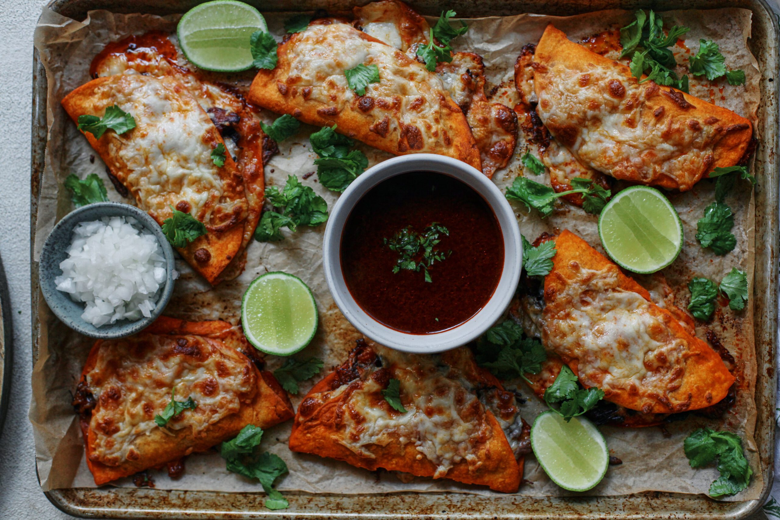 birria sheet pan tacos + a bowl of consomme dressed with cilantro, lime wedges, and a bowl of chopped white onions