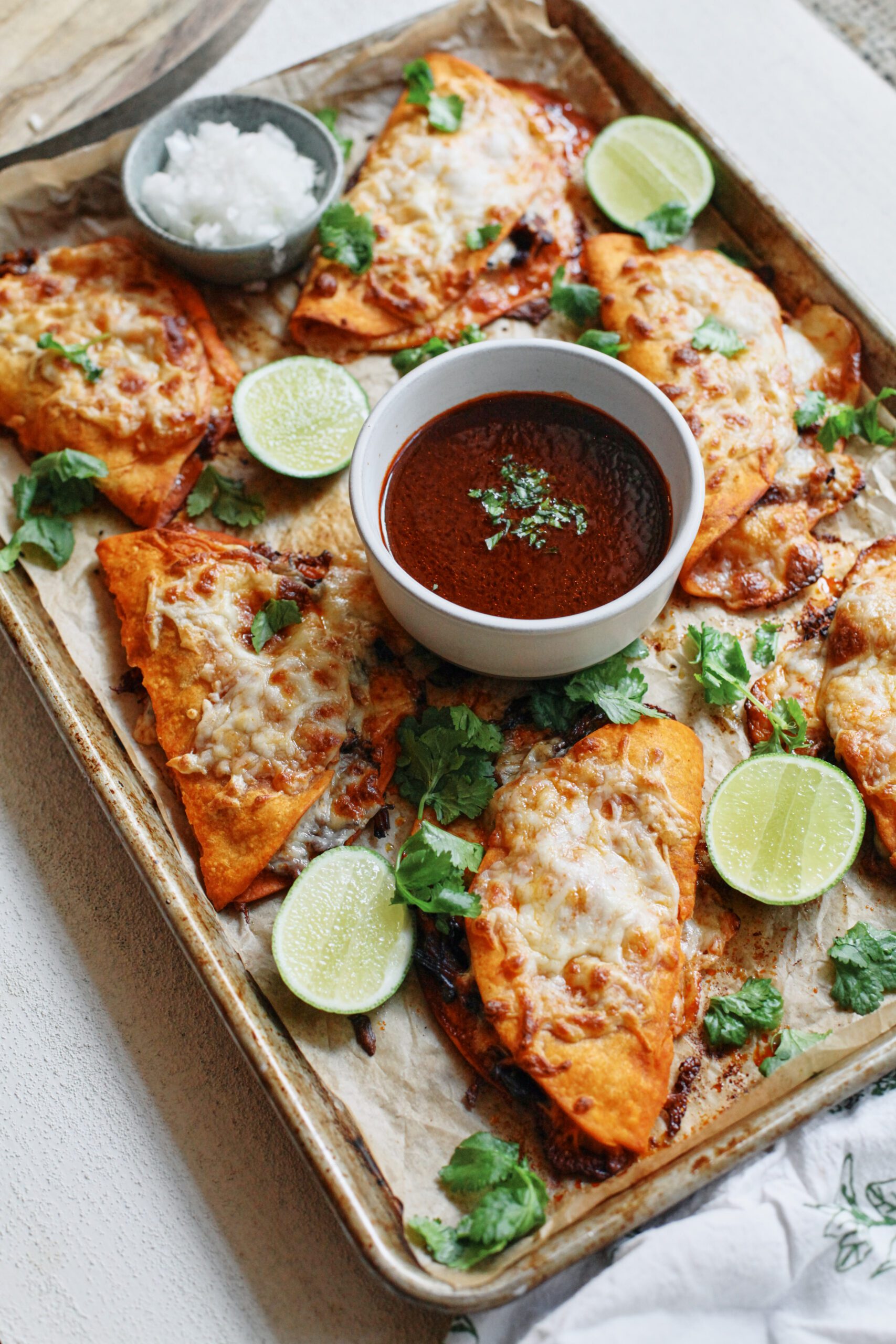 birria sheet pan tacos + a bowl of consomme dressed with cilantro, lime wedges, and a bowl of chopped white onions