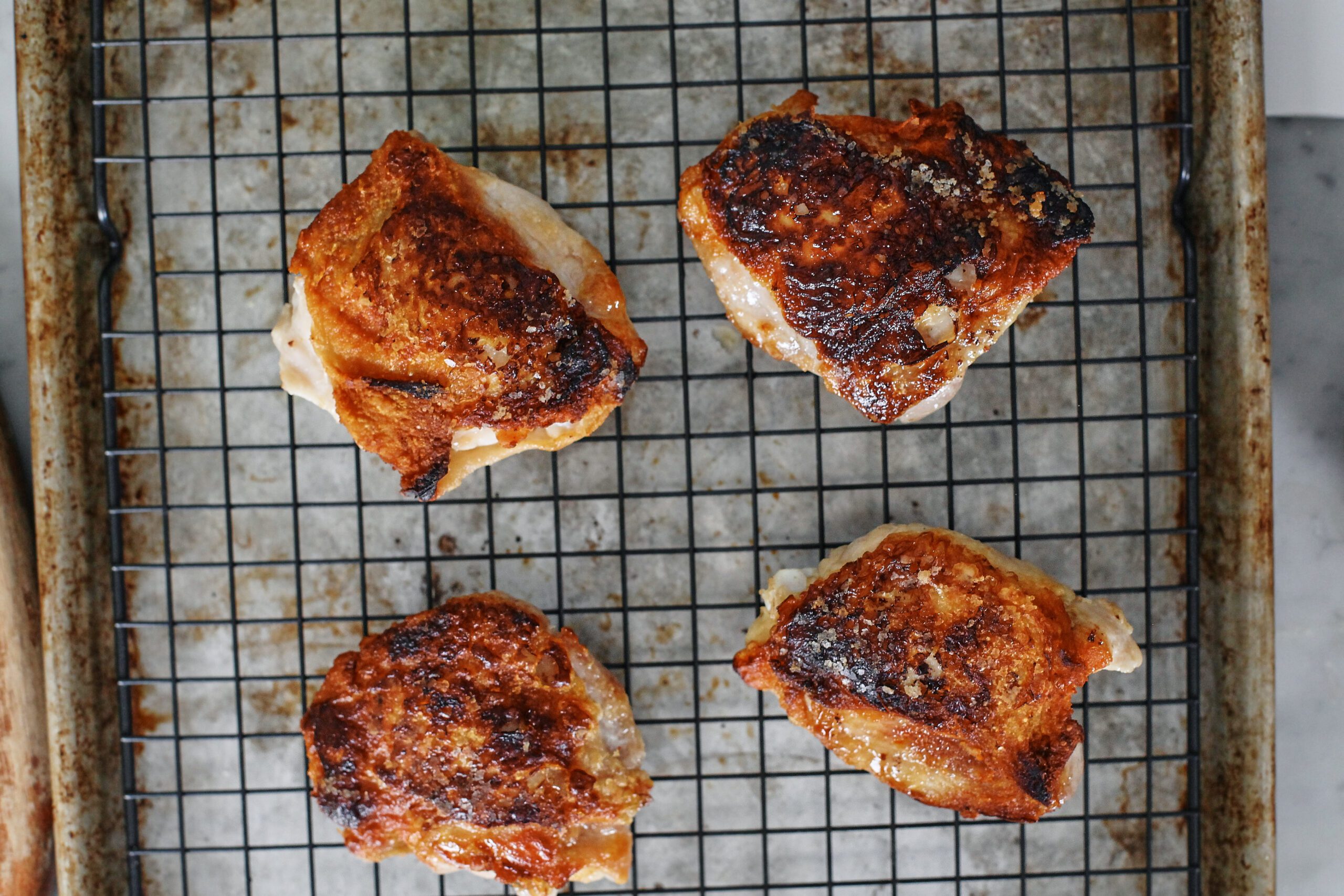 4 seared chicken thighs on a wire rack over a sheet pan