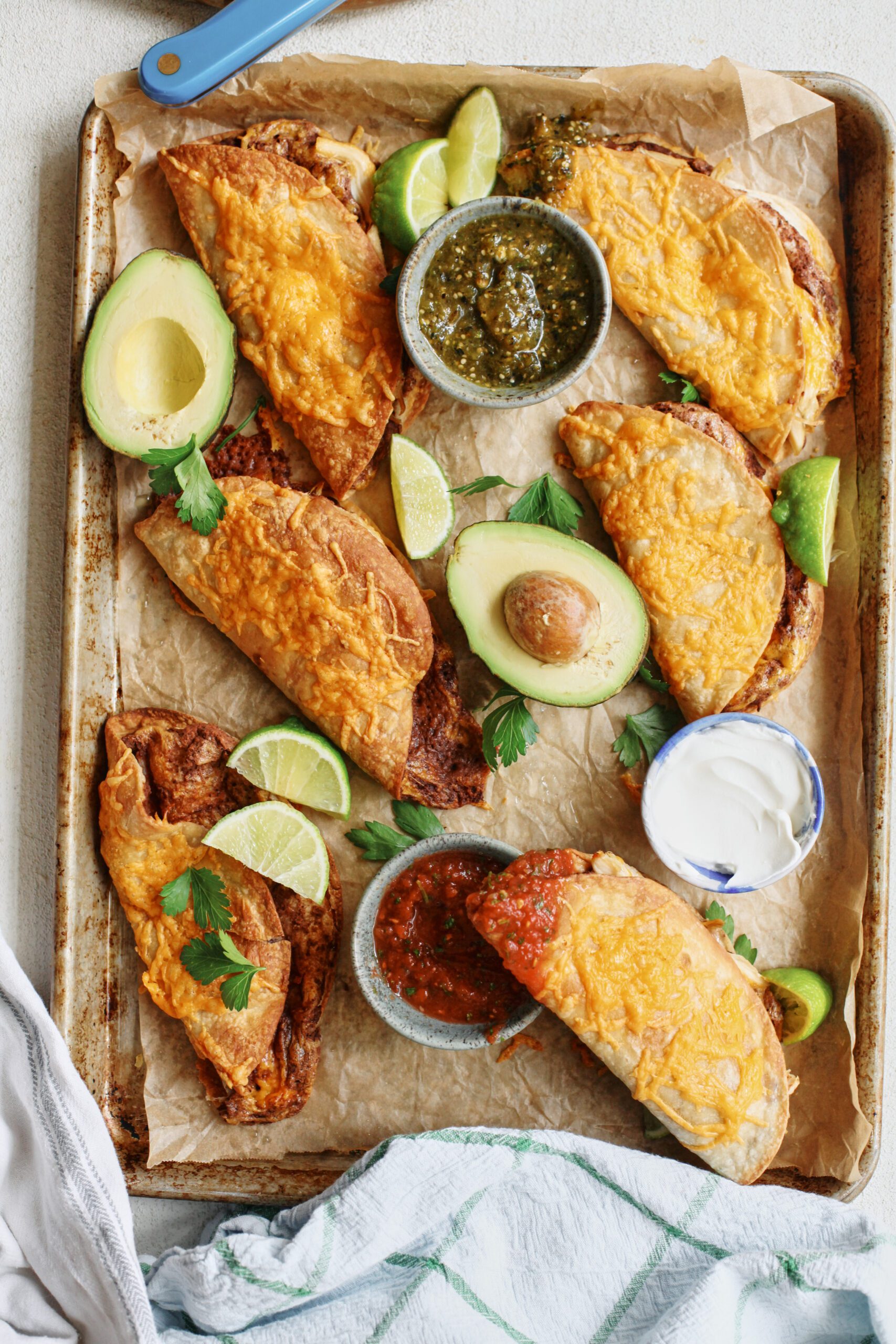 black bean sheet pan tacos arranged on a sheet pan with bowls of red and green salsa, lime wedges, a halved avocado, and cilantro