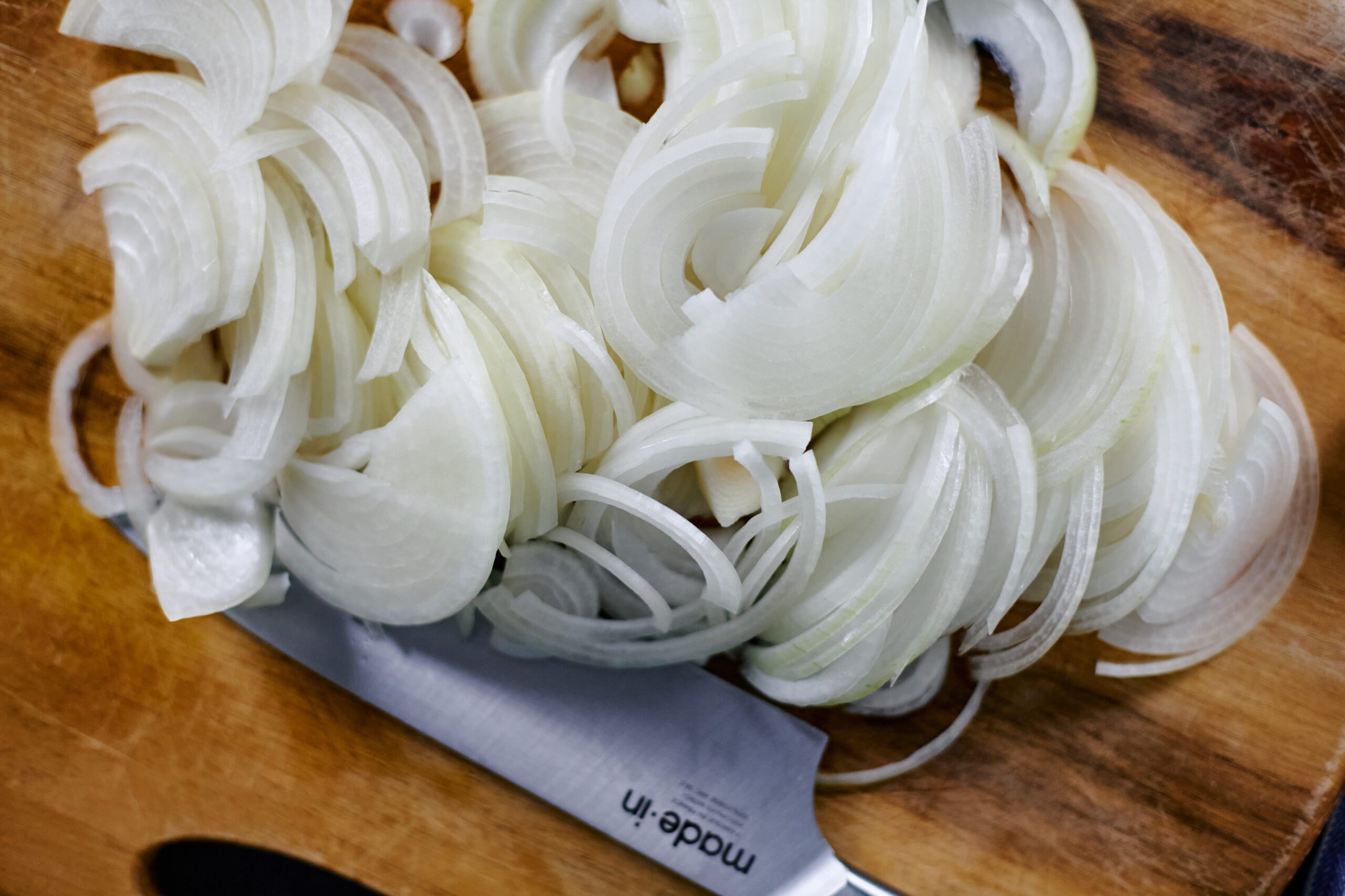 2 thinly sliced yellow onions on a wood cutting board with a chef's knife