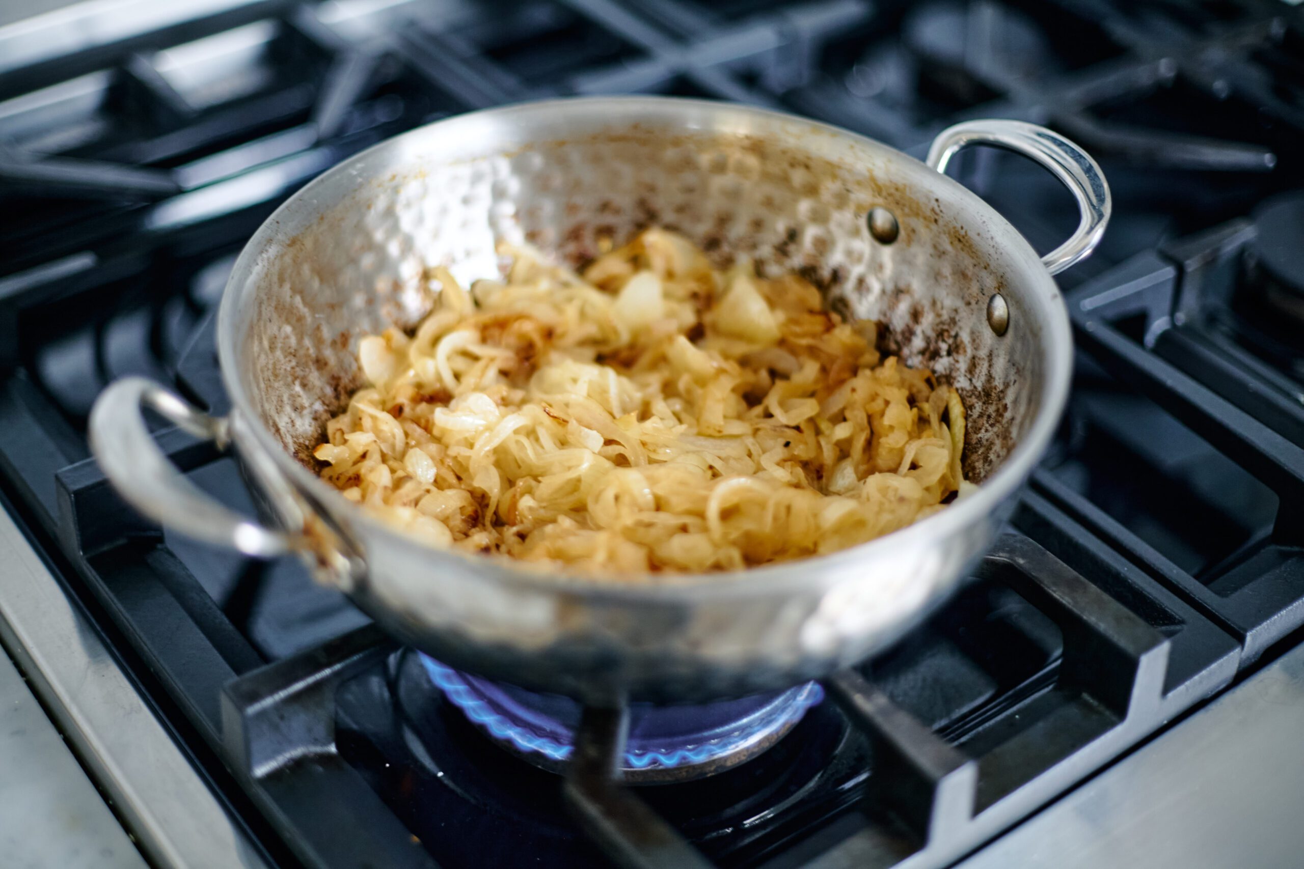 sliced onions sautéing in a hammered steel pan on a gas range