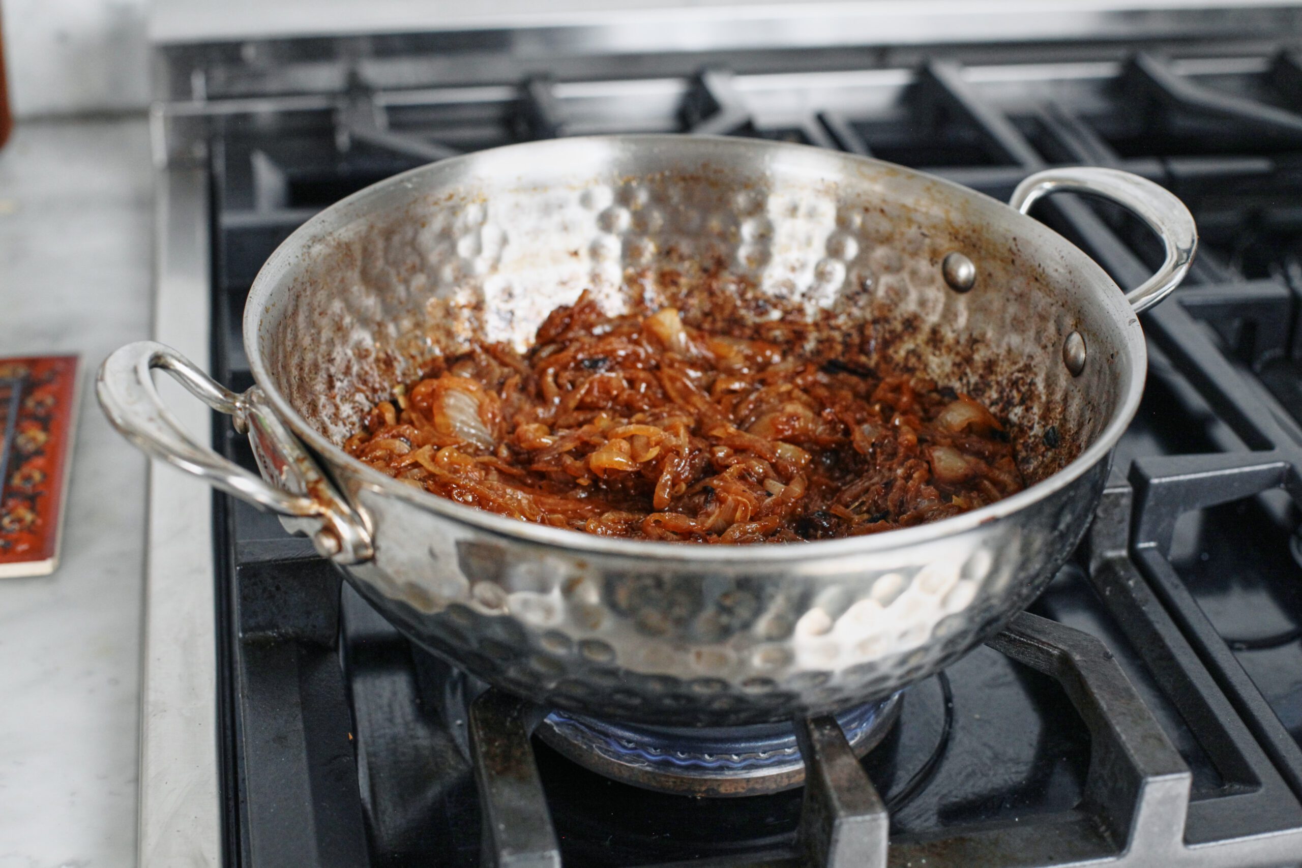 sliced onions caramelizing in a hammered steel pan on a gas range