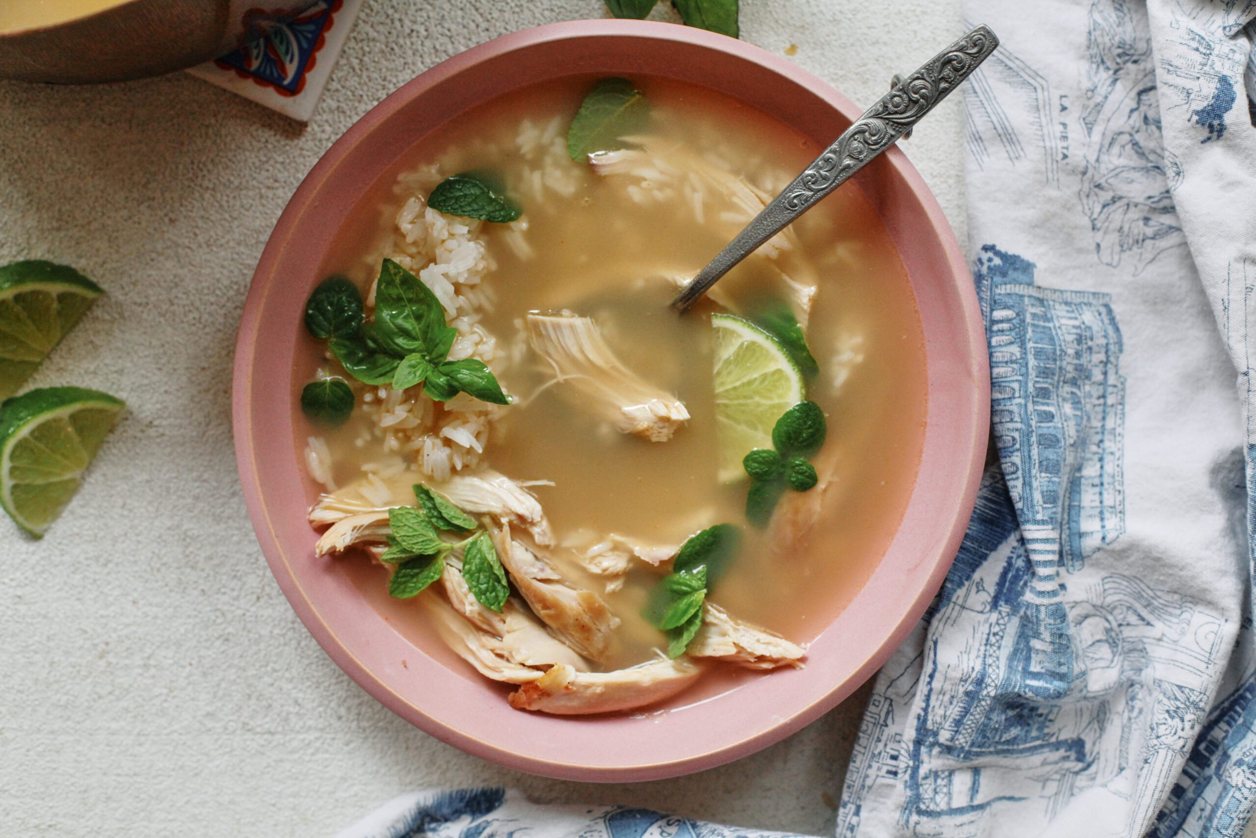 Overhead photo of a bowl of ginger chicken rice soup with shredded rotisserie chicken, fluffy white rice, and fresh mint and basil on top, garnished with a lime wedge