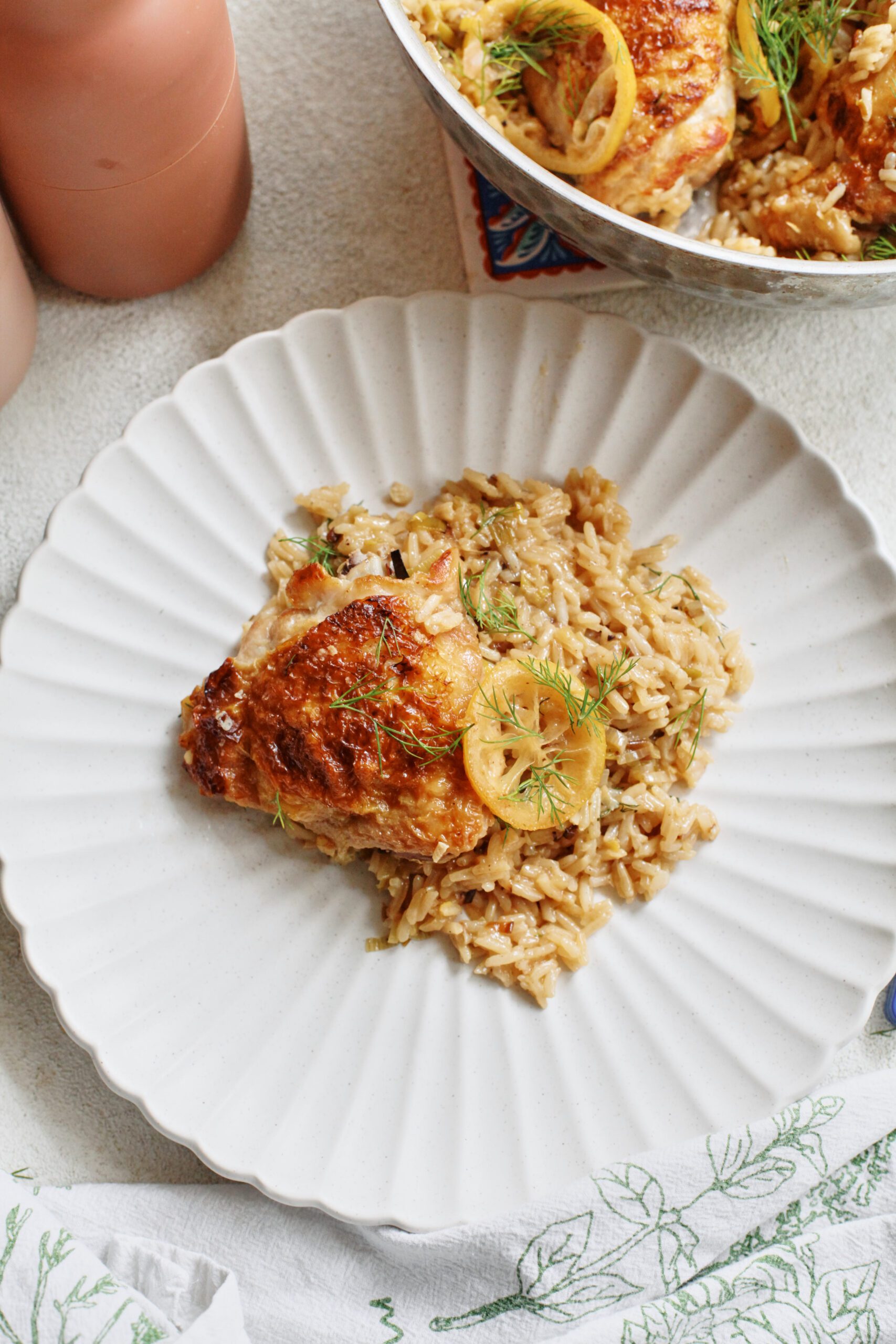 a chicken thigh served over rice, garnished with a seared lemon slice and fresh dill, served on a white plate with scalloped edges