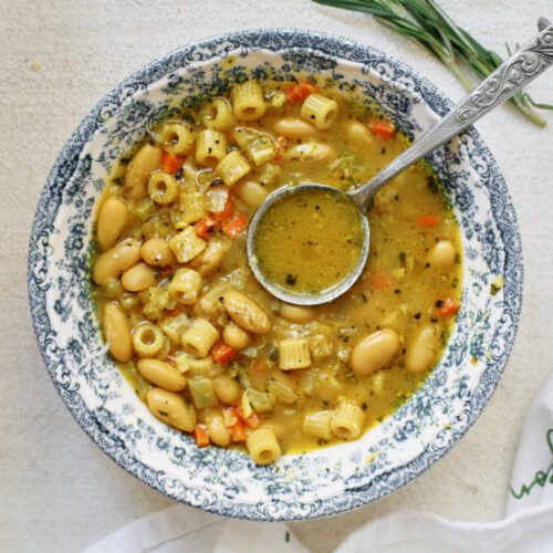 overhead photo of pasta e fagioli alla bianca in a blue/white floral patterned bowl. an antique-looking silver spoon is in the bowl