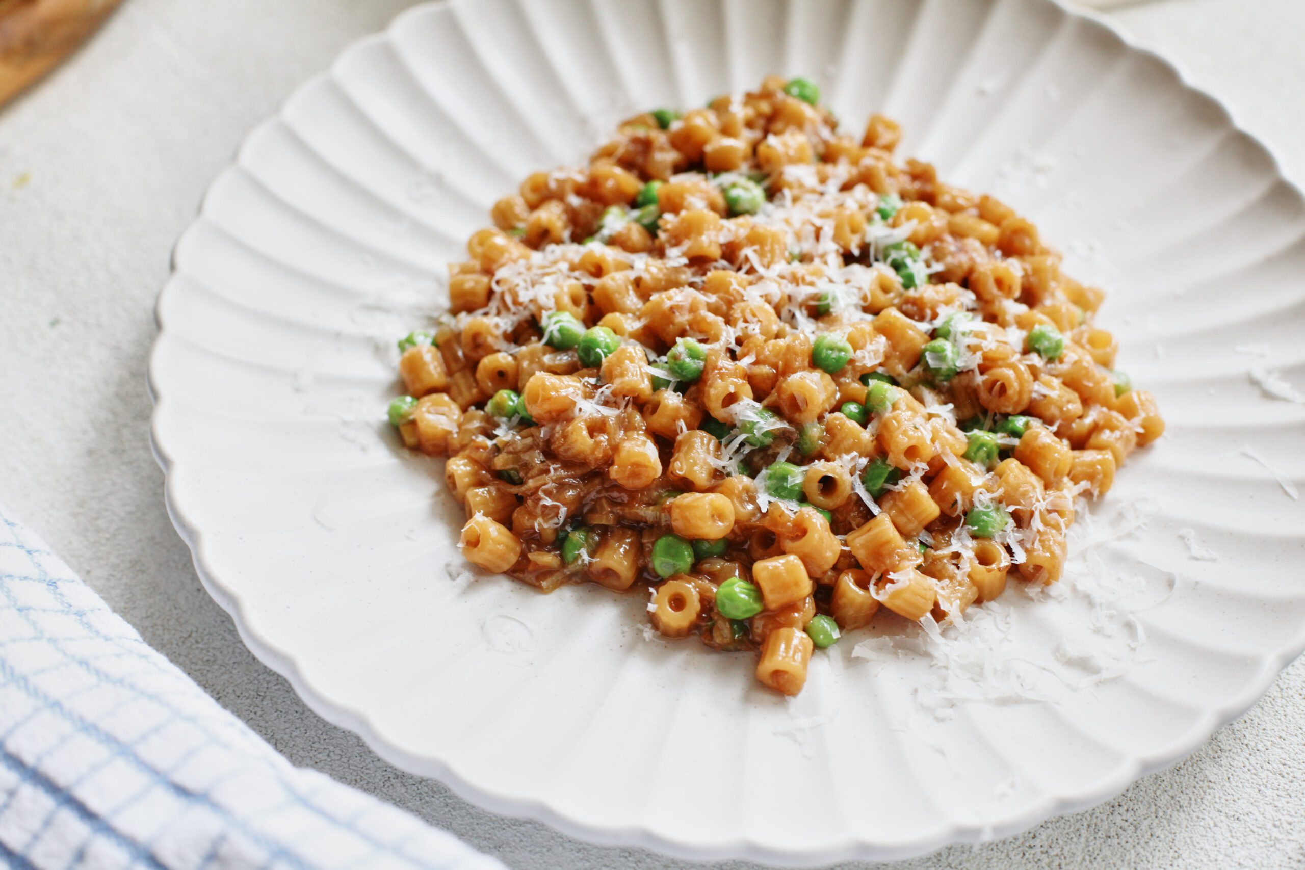 overhead photo of caramelized shallot ditalini with peas on a white plate