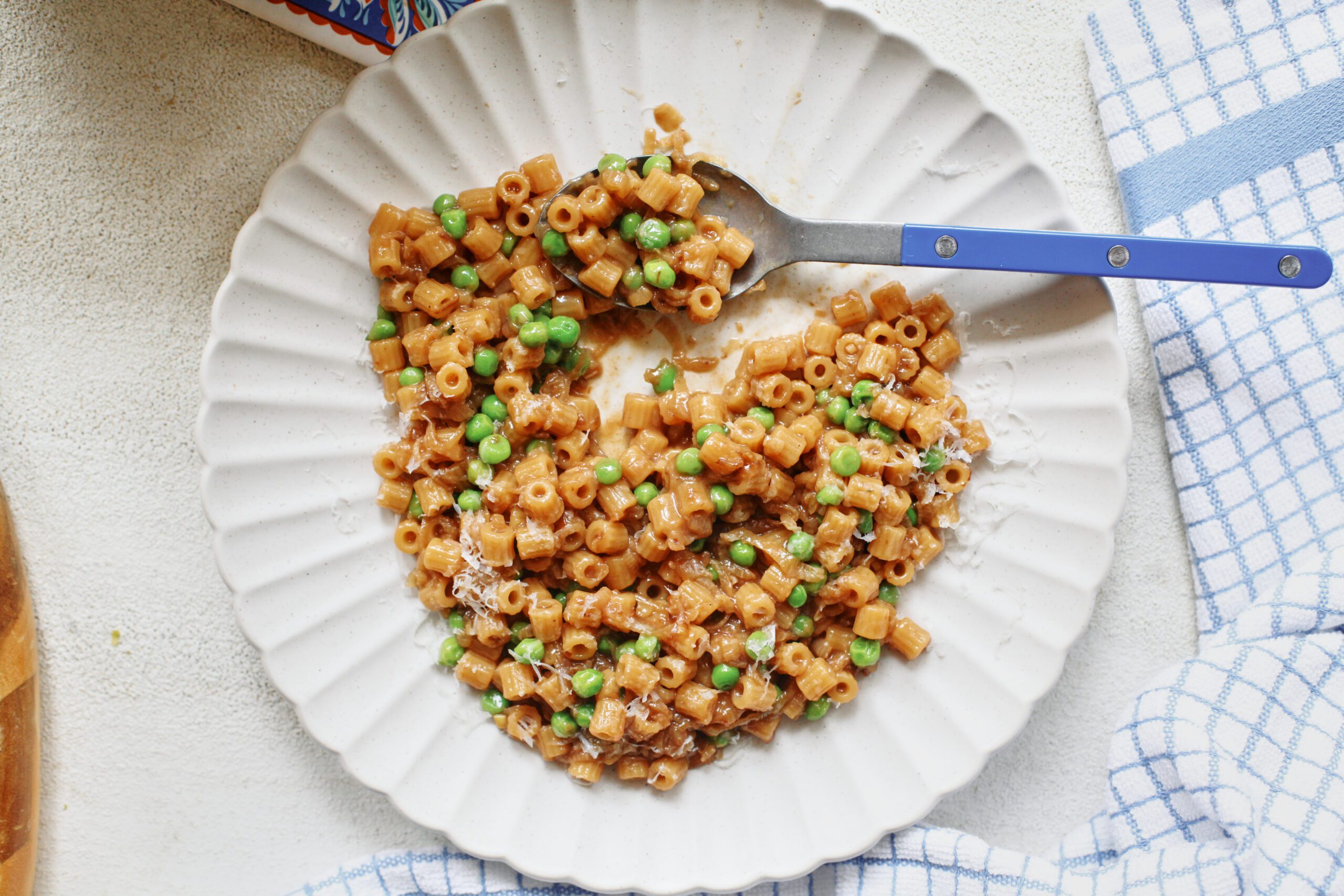 overhead photo of caramelized shallot ditalini with peas on a white plate with a blue spoon