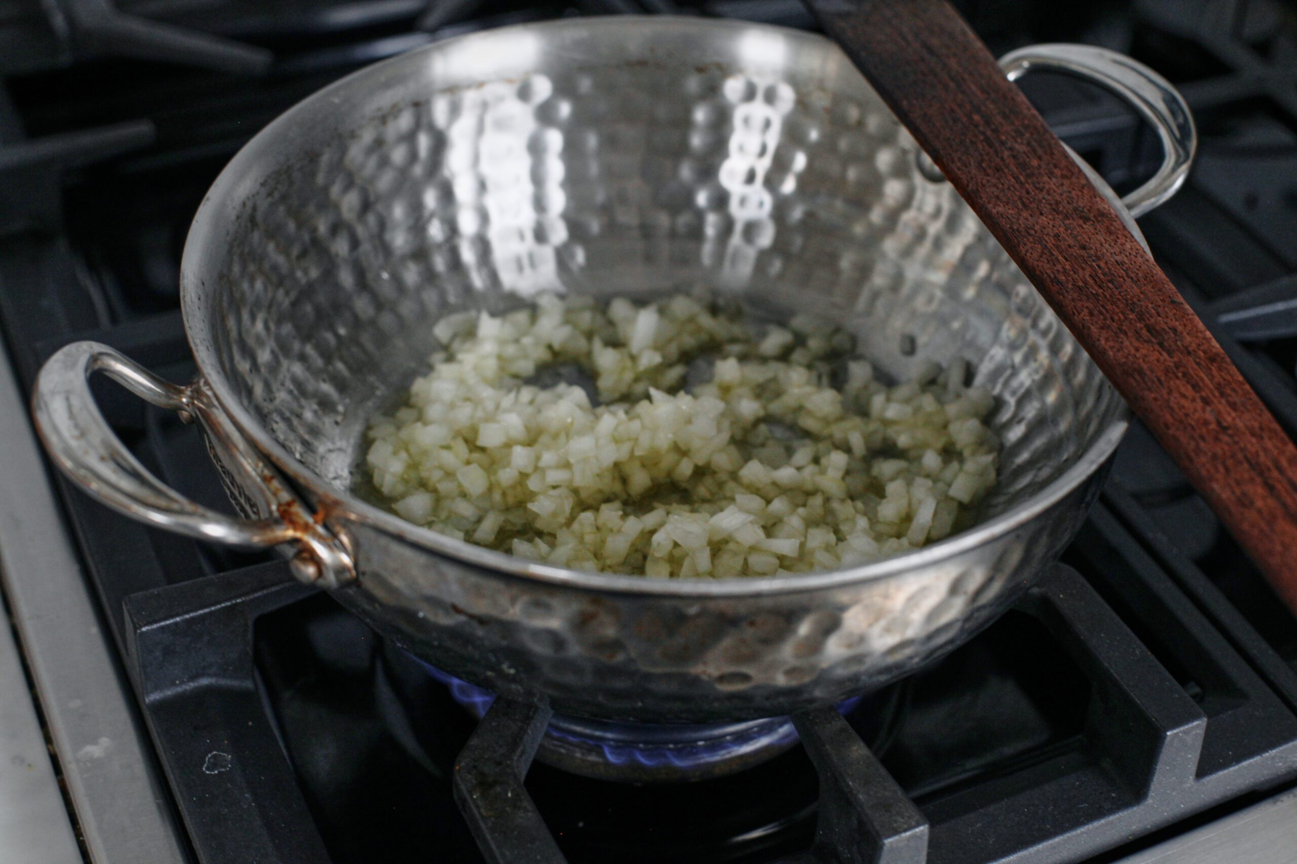 diced onion sauteing in a hammered steel pan